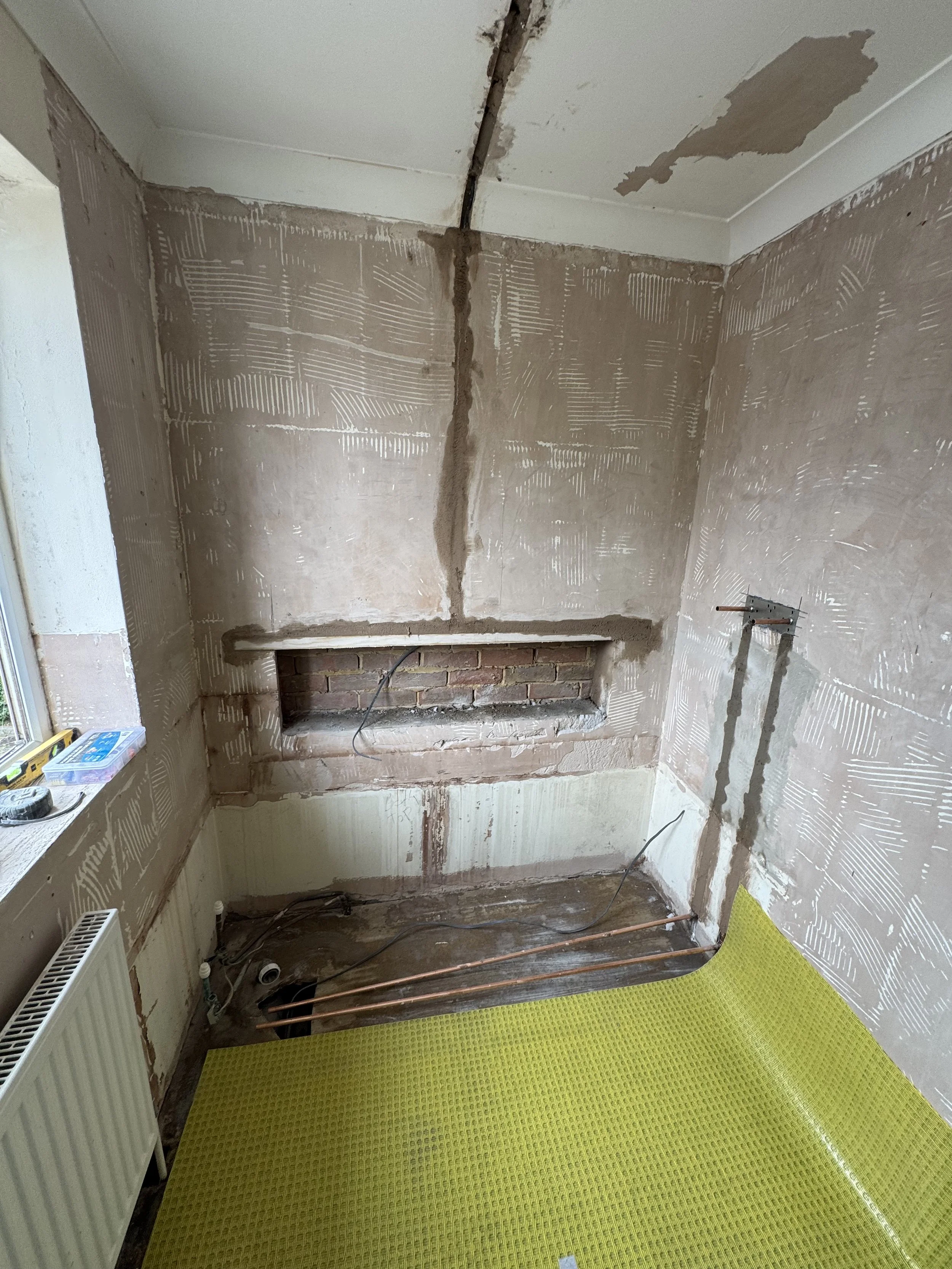 Room undergoing renovation with exposed brick and plumbing, drywall partially finished, and a yellow protective floor covering.