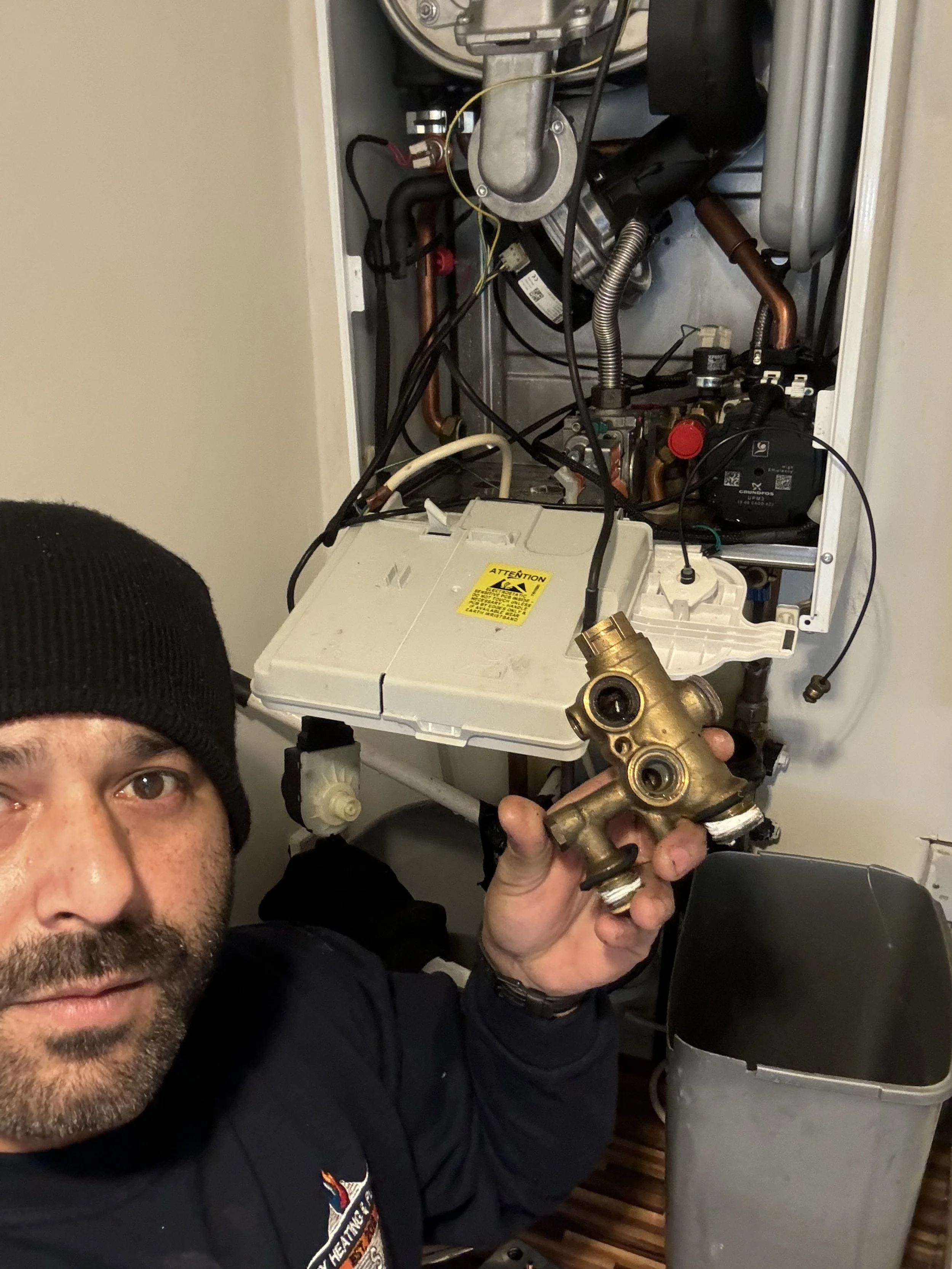 Technician holding a brass valve part in front of an open furnace or boiler with internal components and wiring.