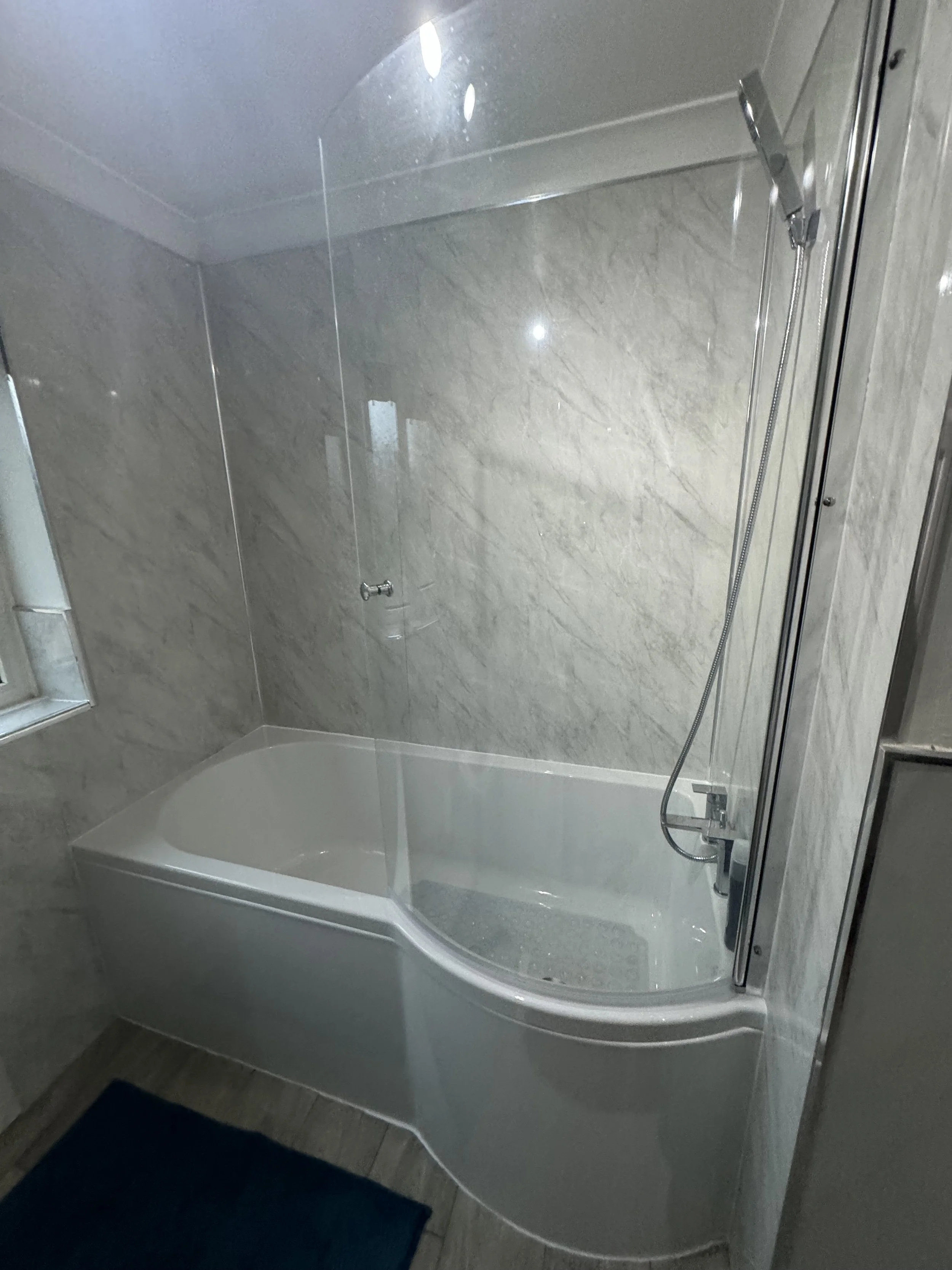 Bathroom with a bathtub, glass shower partition, and beige marble walls.