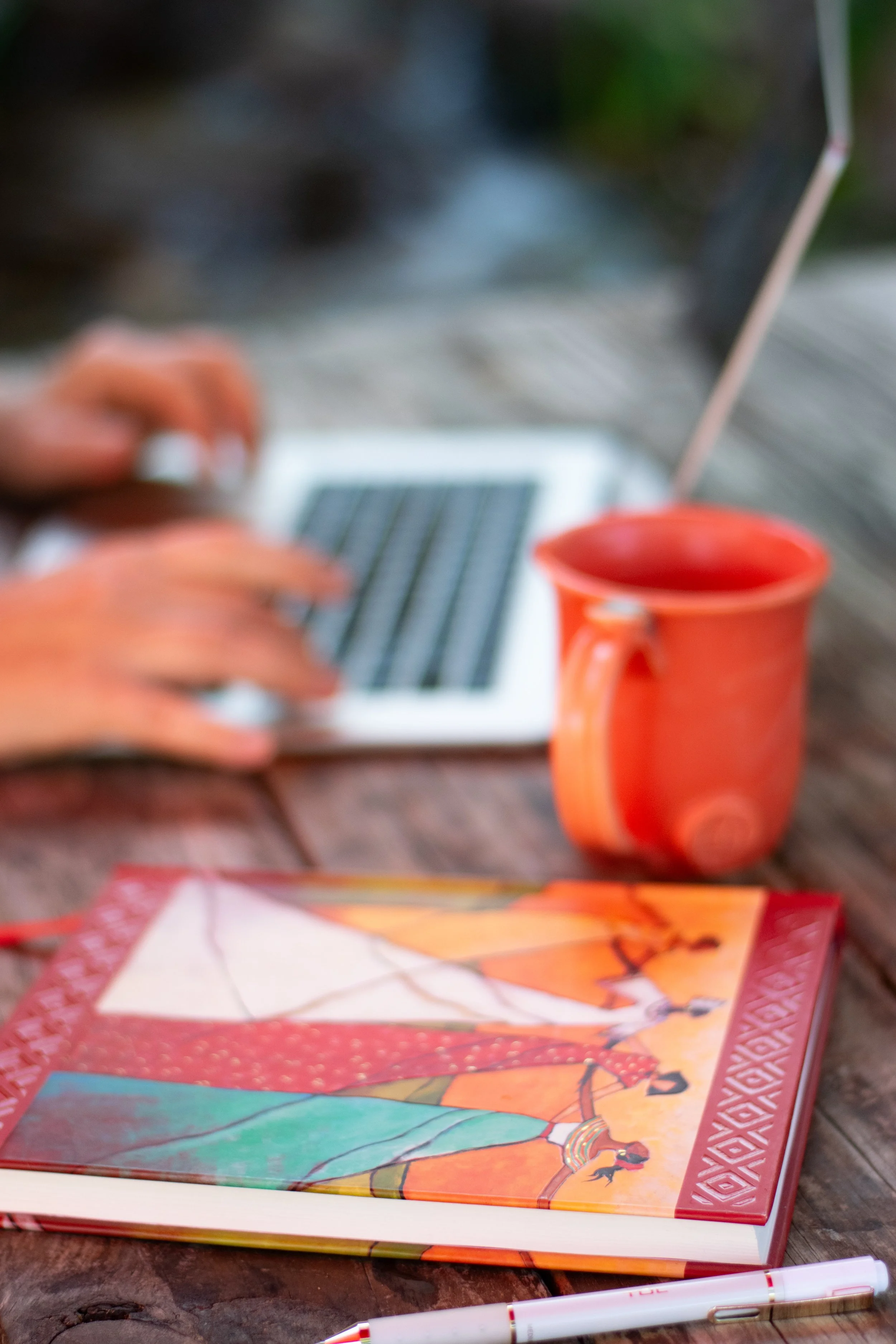 Person on their computer with an orange ceramic coffee mug by their side.