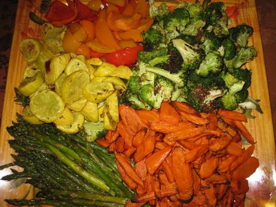 Assorted chopped vegetables on a wooden cutting board, including broccoli, carrots, asparagus, bell peppers, and yellow zucchini.