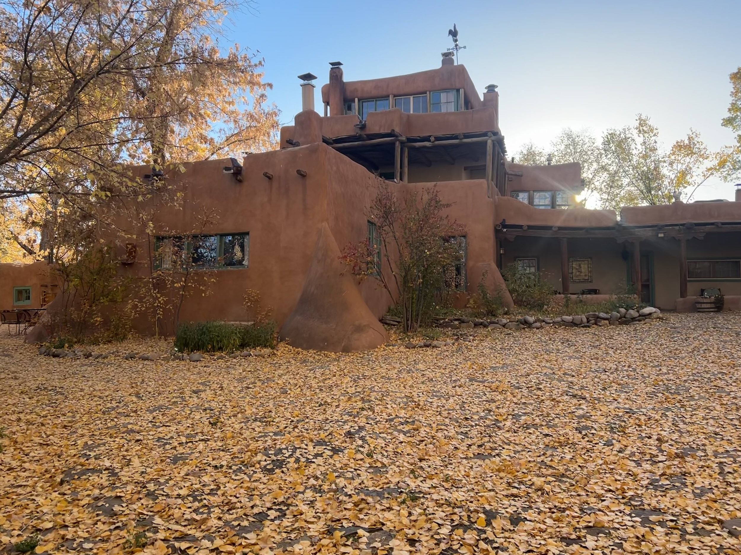 tan stucco home surrounded by golden trees with the rising sun peeking over the backside of the home.