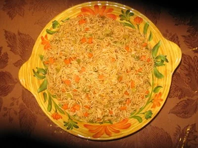 A colorful floral bowl filled with cooked rice mixed with chopped carrots and peas placed on a patterned tablecloth.