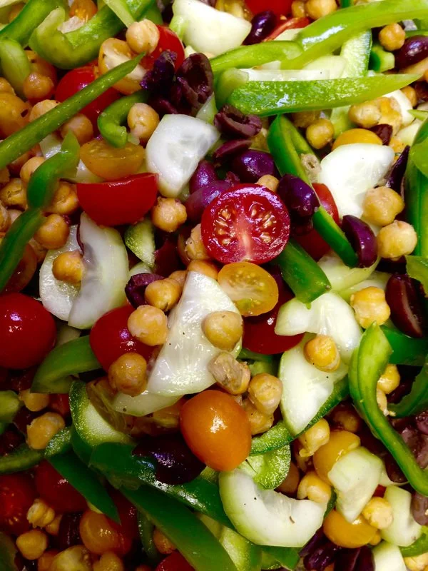 Close-up of a colorful vegetable salad with cherry tomatoes, chickpeas, cucumbers, green peppers, and black beans.