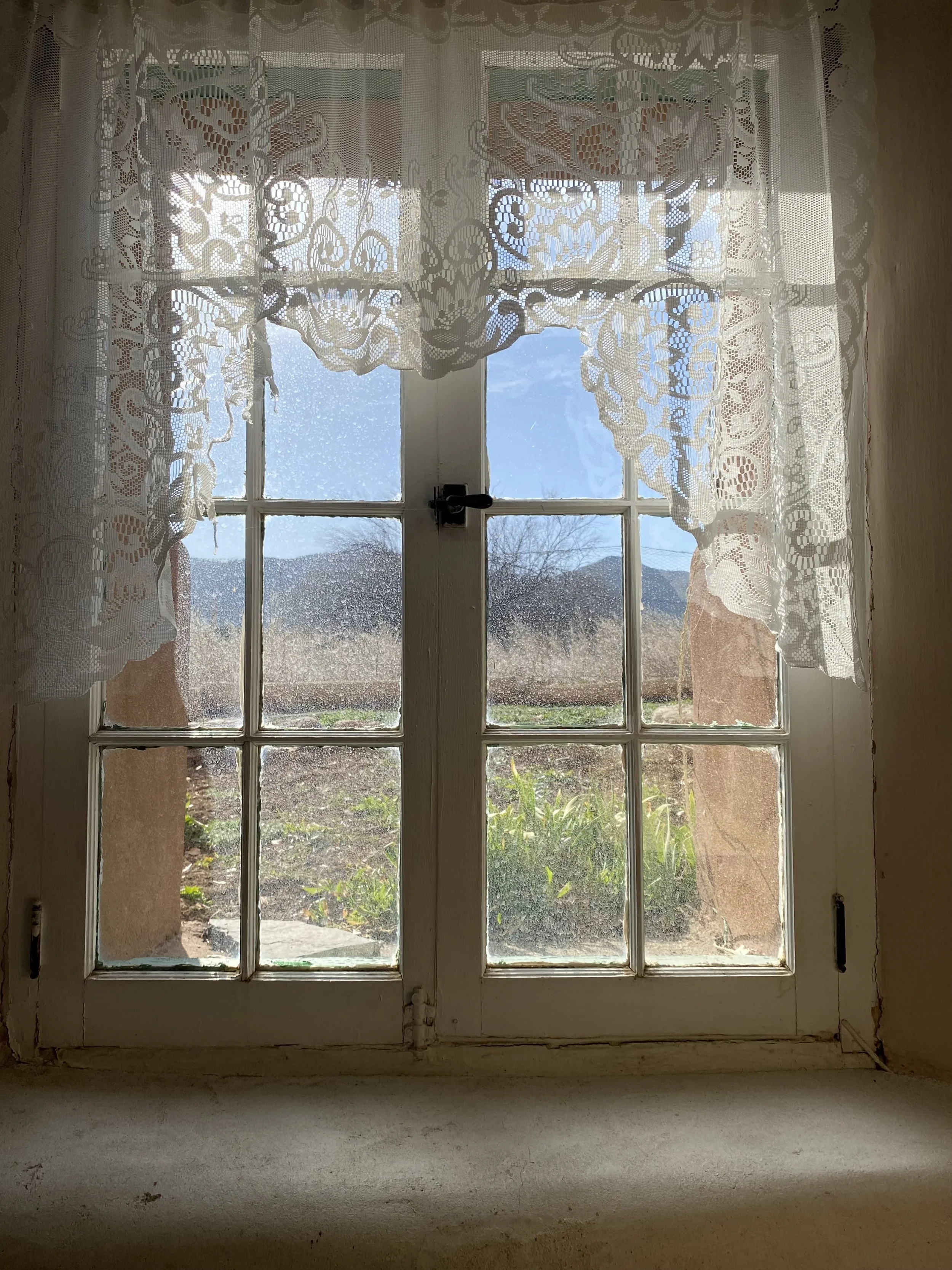 Inside shot, looking outside, through old with Juliet windows. Draped with white lace and outside is the view of mountains in the distance.