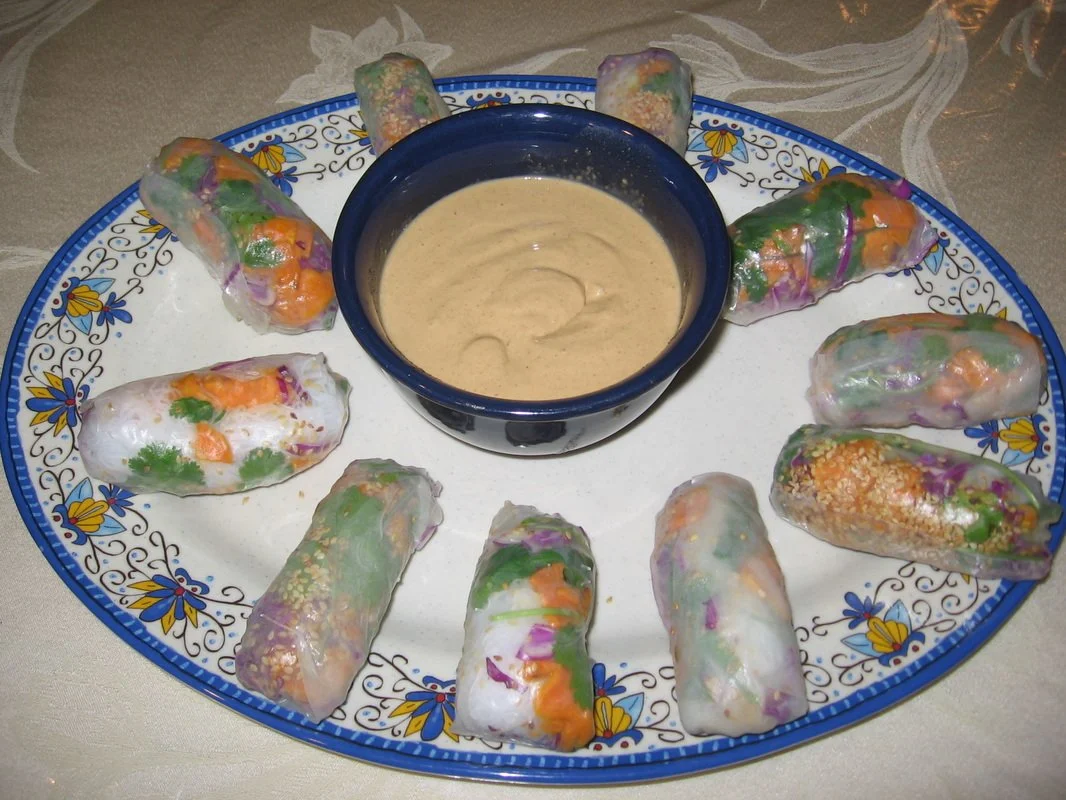 A decorative blue and white platter with ten Vietnamese spring rolls arranged around a small blue bowl of dipping sauce in the center.