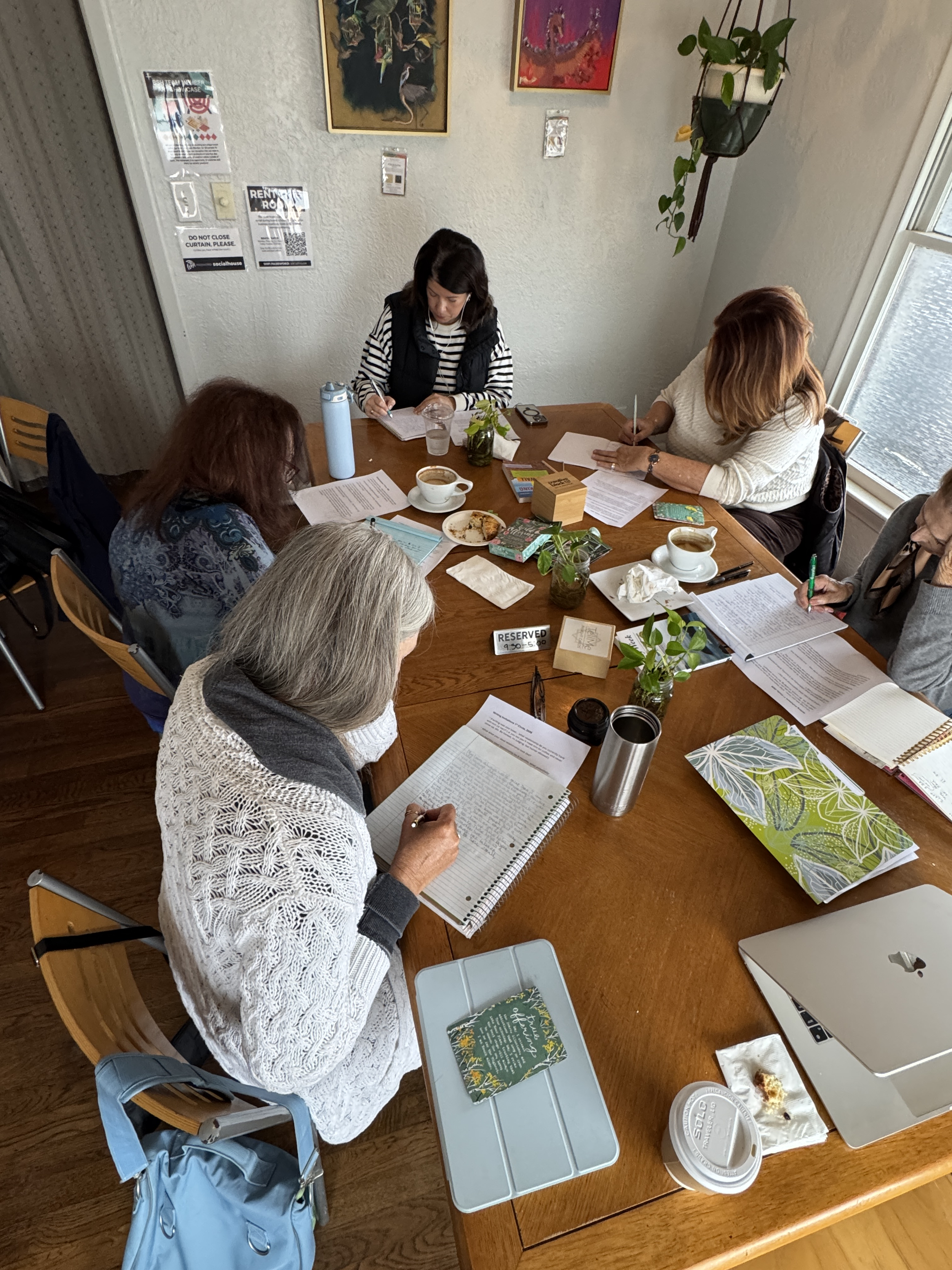 Group of women at a coffee table write together intensely..