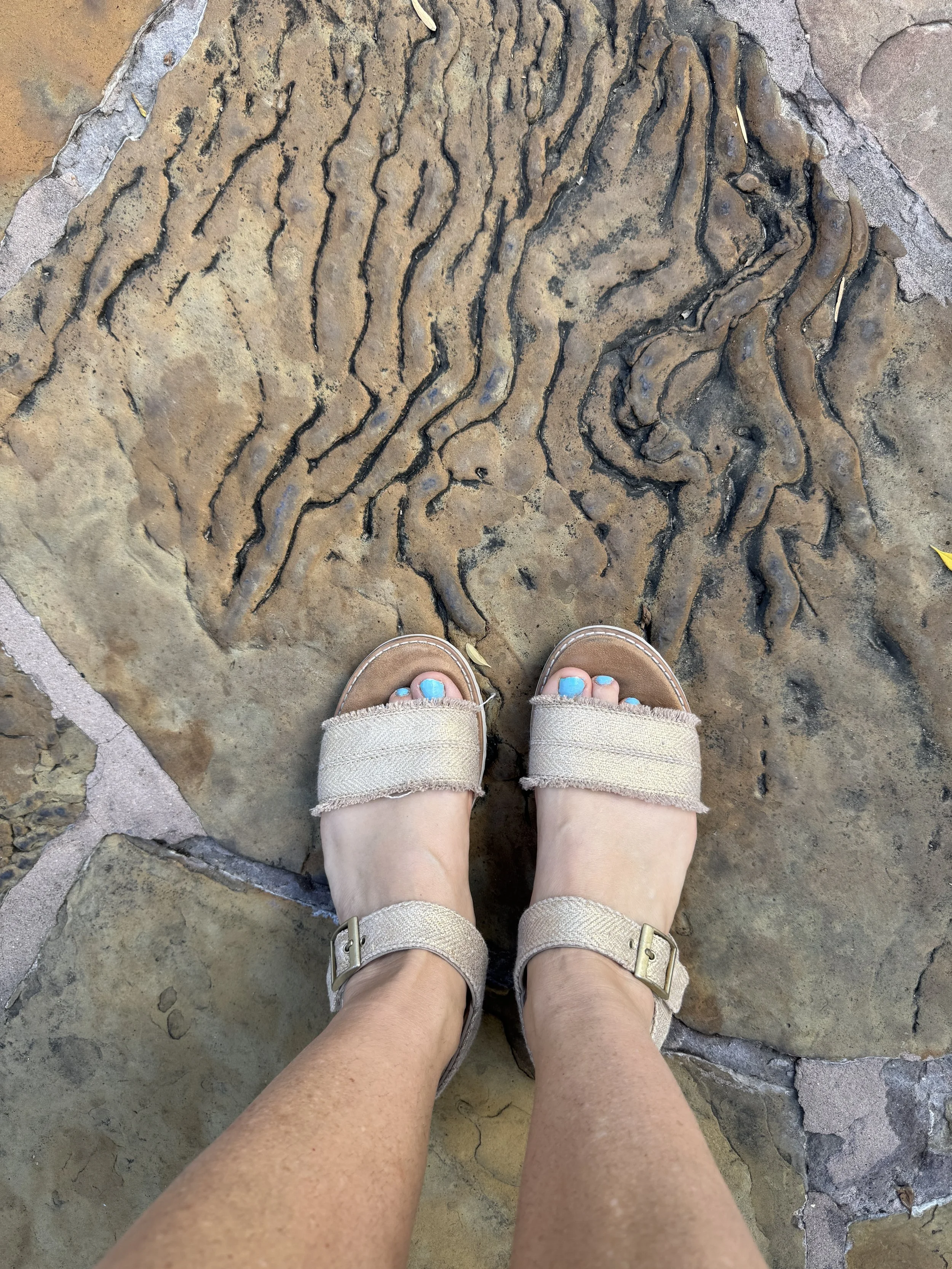 Overhead shot of feet, with sandals, stand on top of warped stone that resemble the ripple of water. Toenails are teal matching the star bullets in the following section.