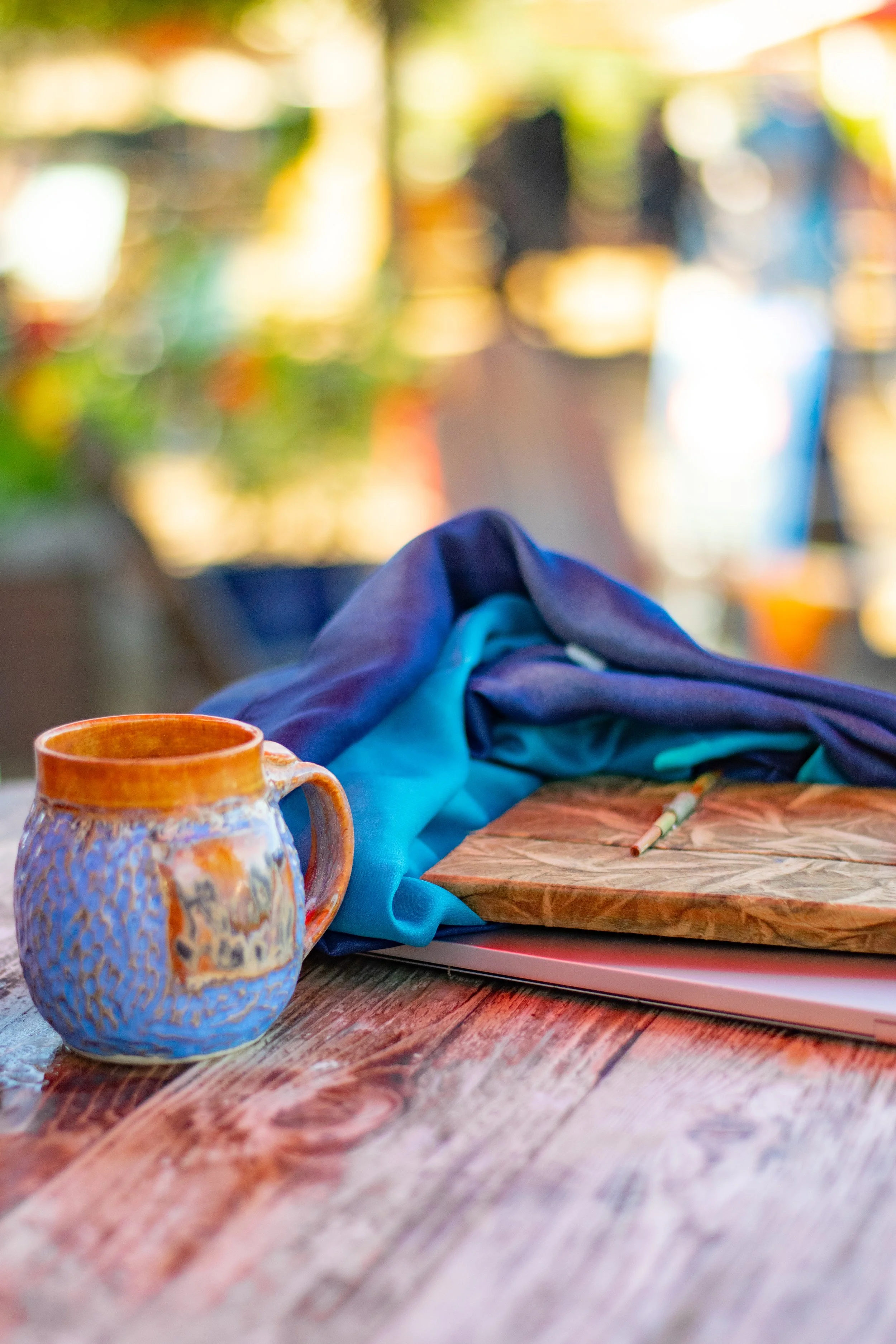 Blue ceramic coffee mug, accompanied by a blue/purple scarf and a journal.