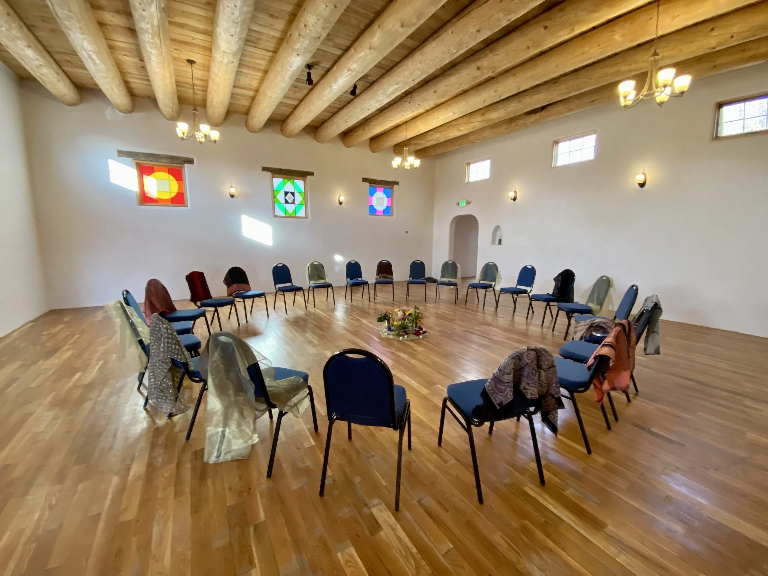 Empty blue chairs surround an altar of thanks-giving. The room is empty with beautiful wooden cieling beams and high stained glass windows, ensuring focus on said activity.