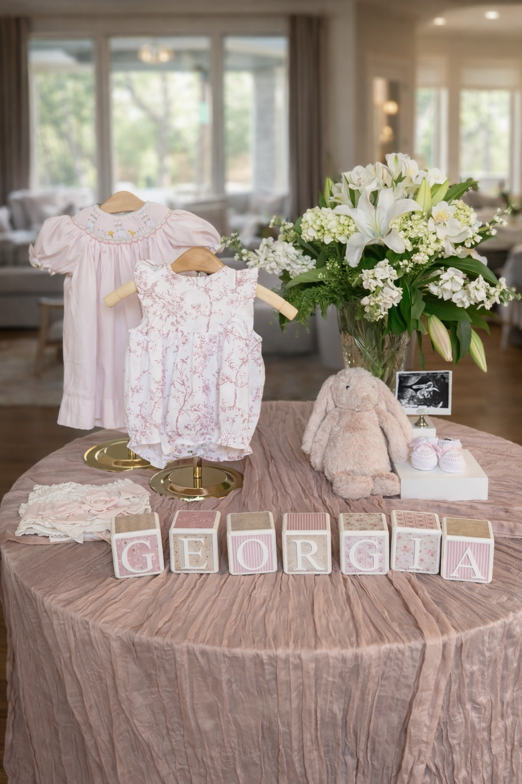 A display featuring baby clothes on hangers with floral designs and a plush toy rabbit. Decorative blocks spell "Georgia".