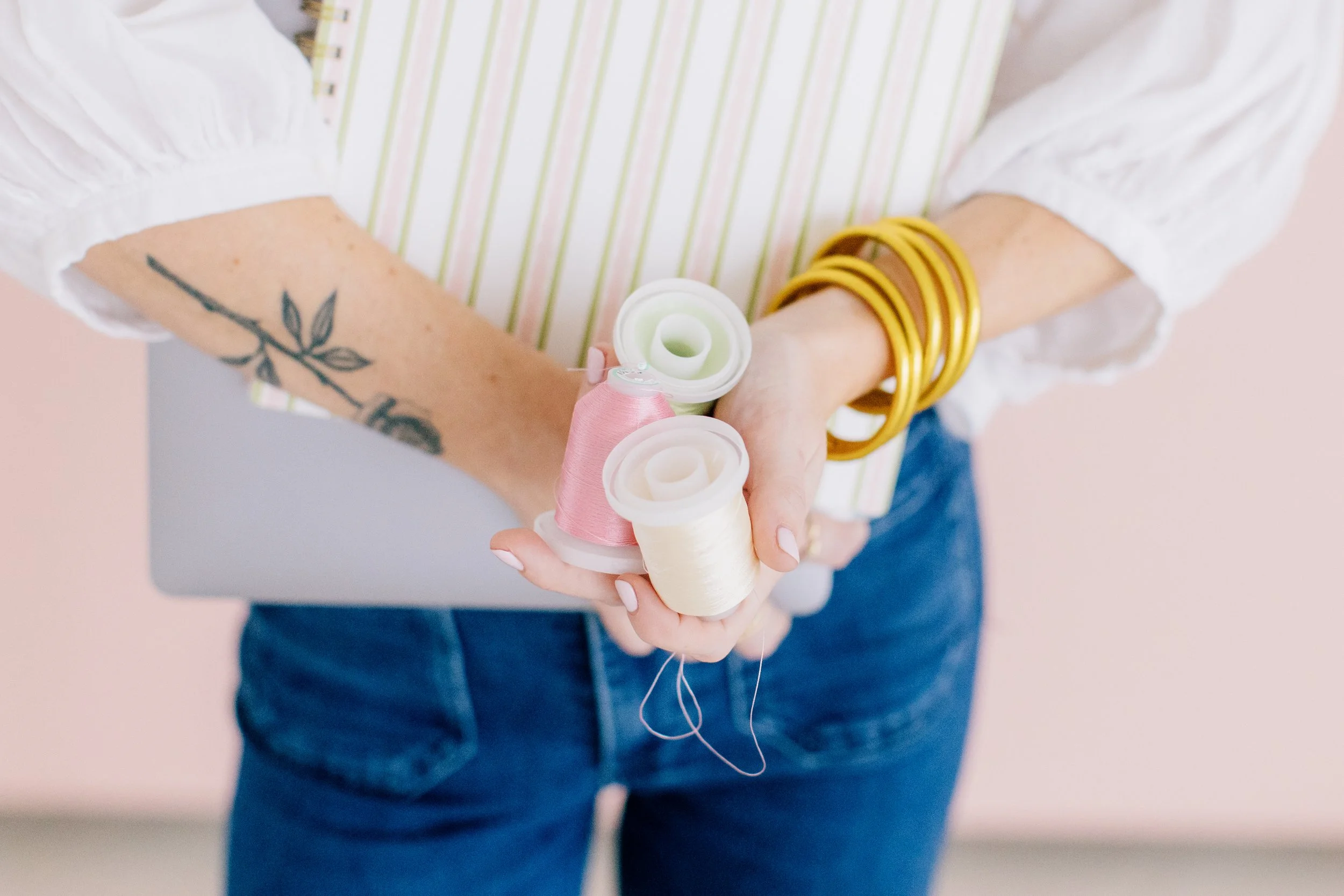 A woman wearing gold bracelets holds light colored spools of thread.