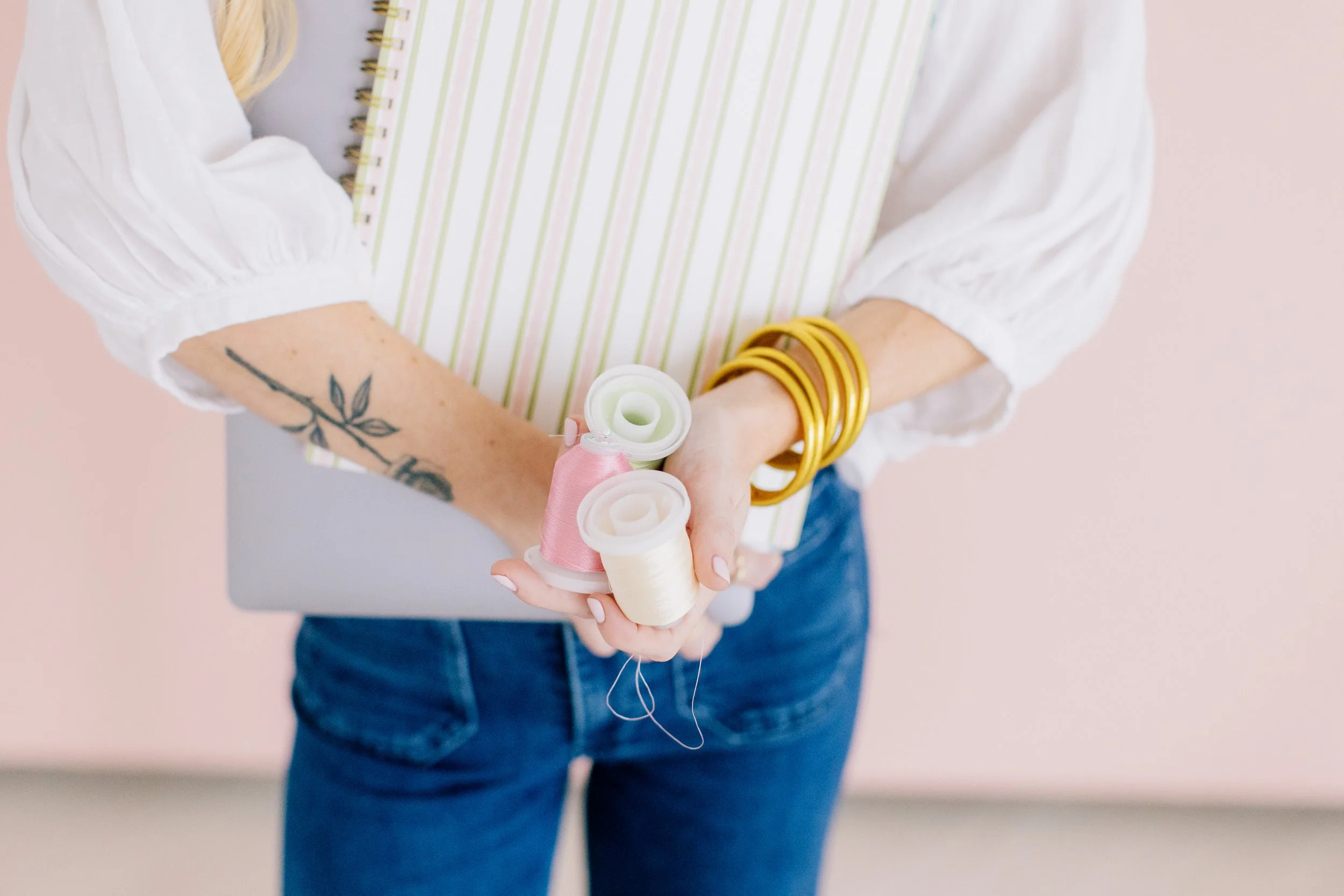 A woman holding white and pink thread spools in her hands with gold bracelets on.