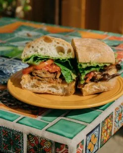 A plate with two sandwiches on a tiled table, one with turkey, lettuce, tomato, and bread, and the other with beef, lettuce, and sandwich bread.