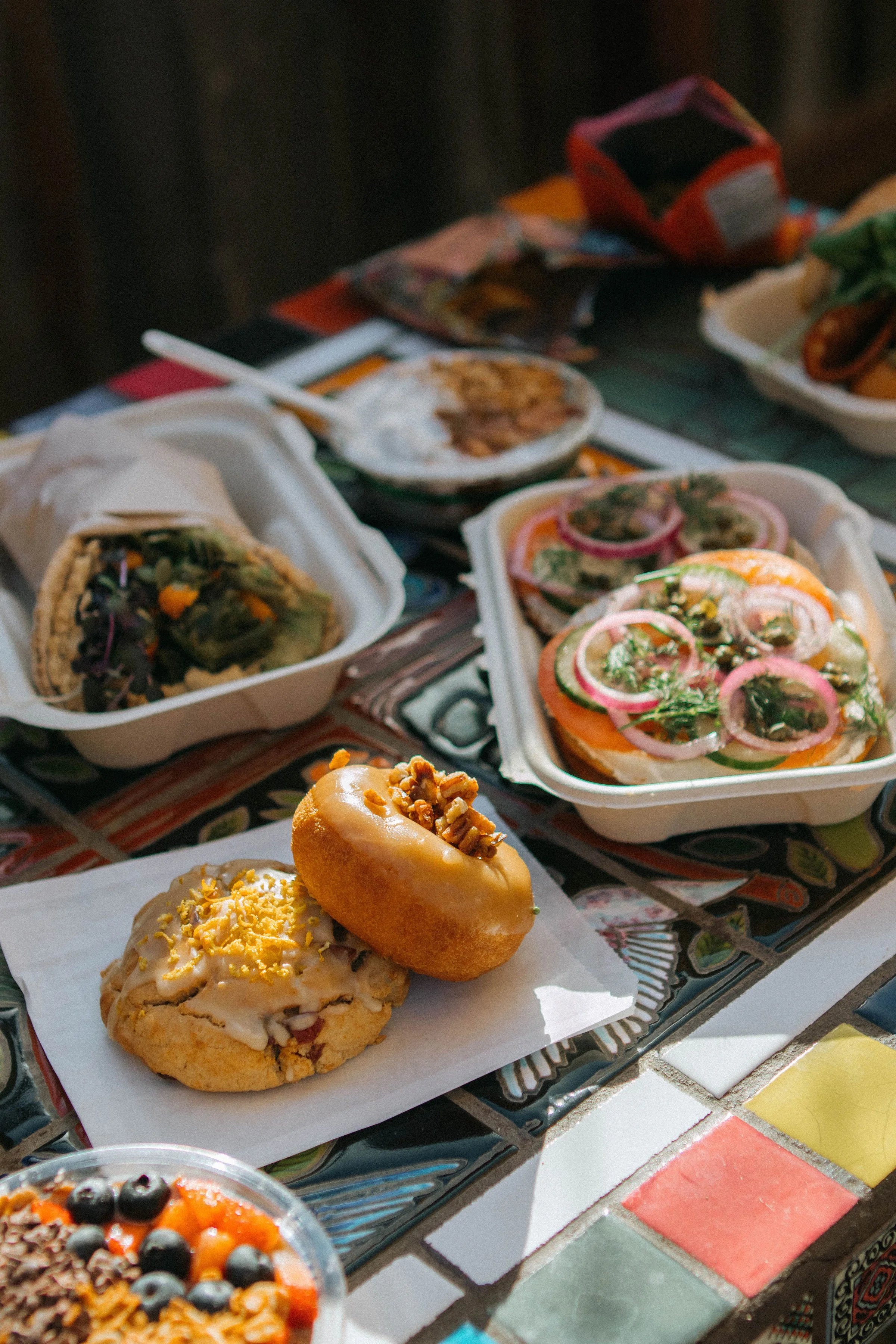 An assortment of Mexican foods including tamales, sopes, and a churro with icing and sprinkles on a colorful table.