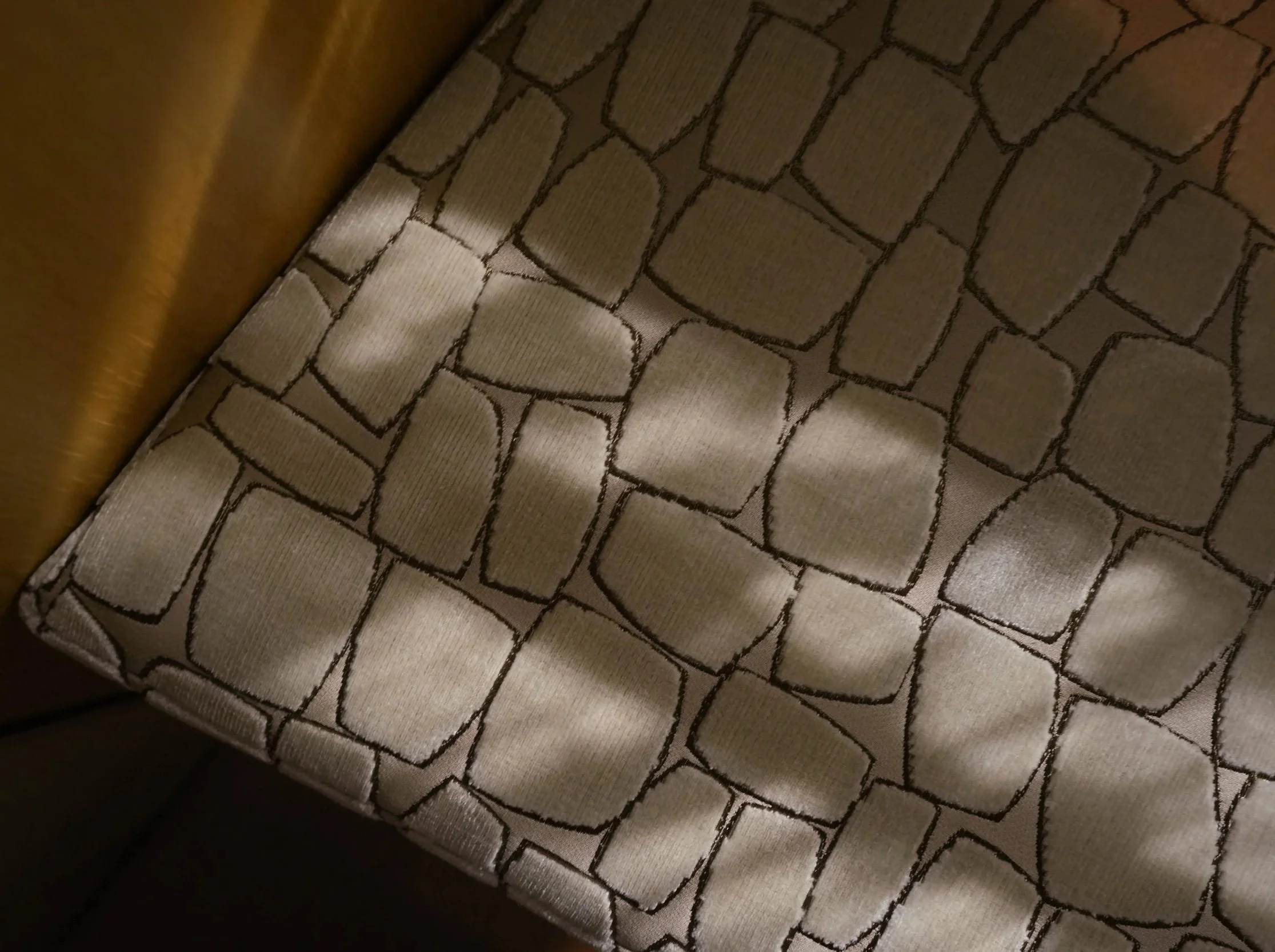 Close-up of a padded, upholstered chair with a cream-colored fabric featuring a geometric pattern of connected rectangles outlined in dark brown.