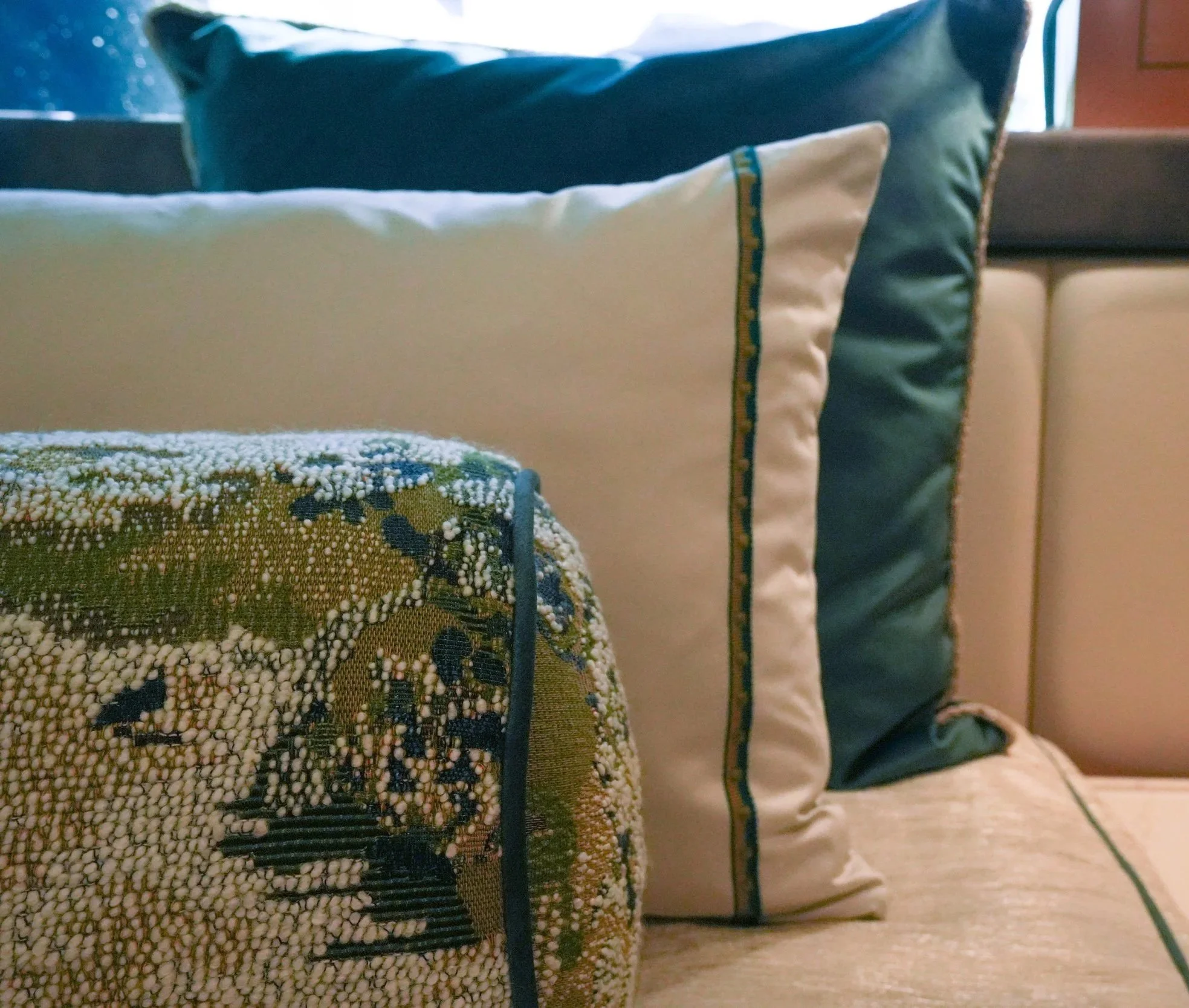 Close-up of a row of decorative pillows on a beige sofa, focusing on a patterned pouch with a textured, speckled surface in the foreground.