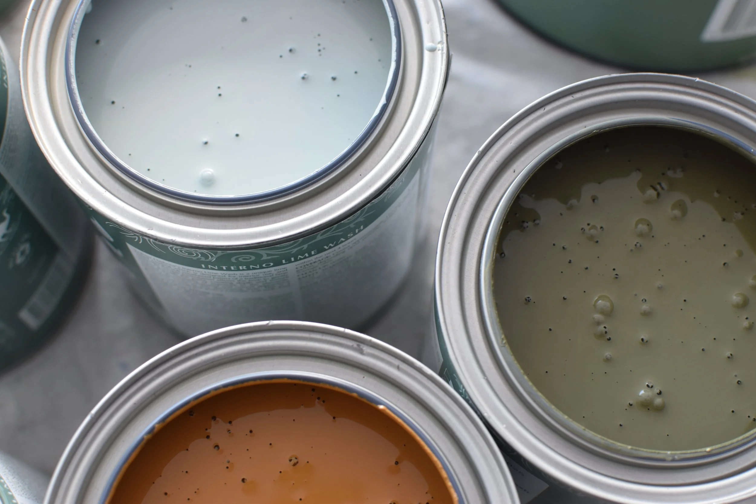 Open cans of cream, green, and brown paint showing paint with bubbles.
