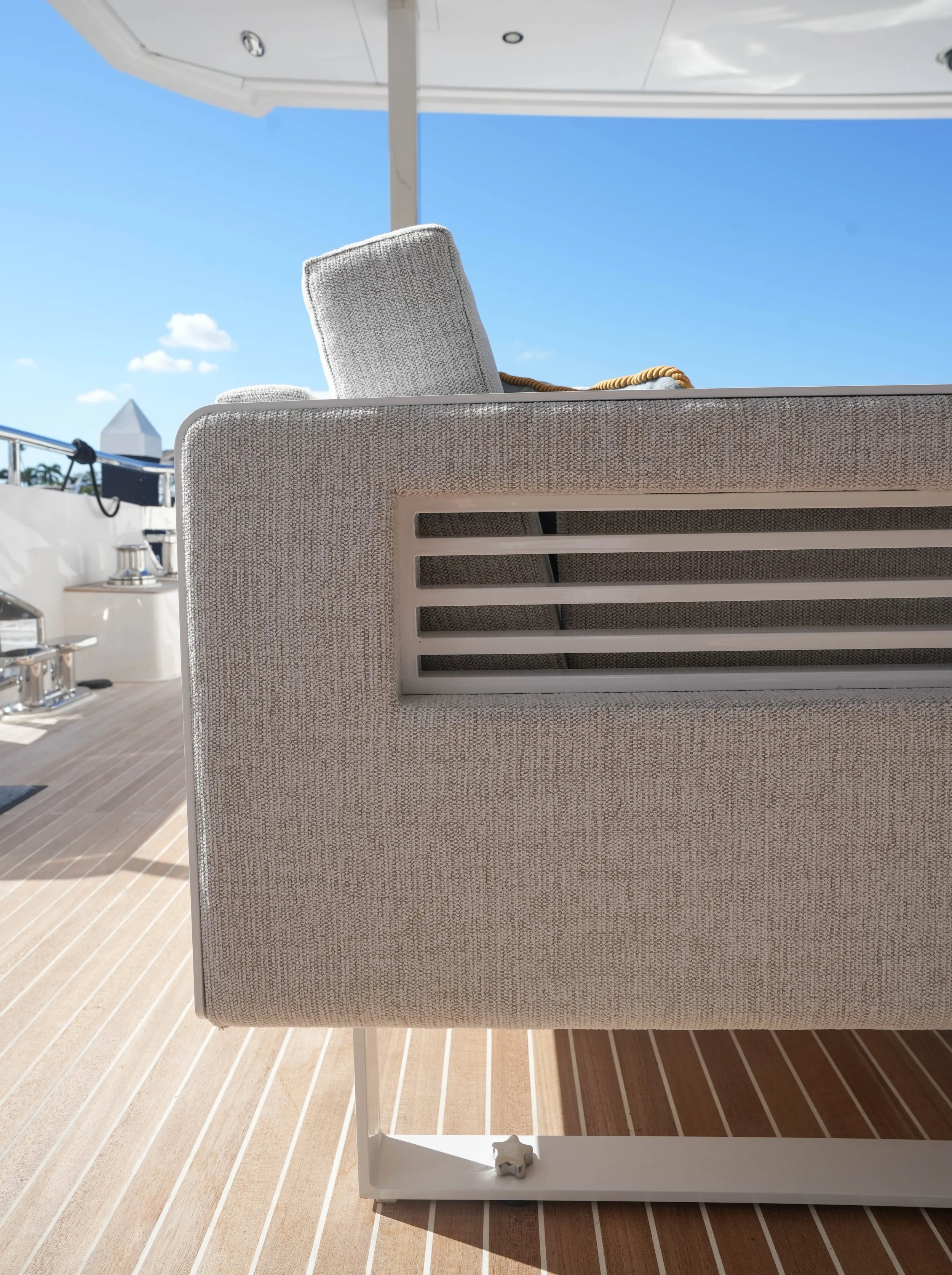 Close-up of a beige upholstered outdoor chair on a yacht deck with a view of the blue sky and clouds in the background.