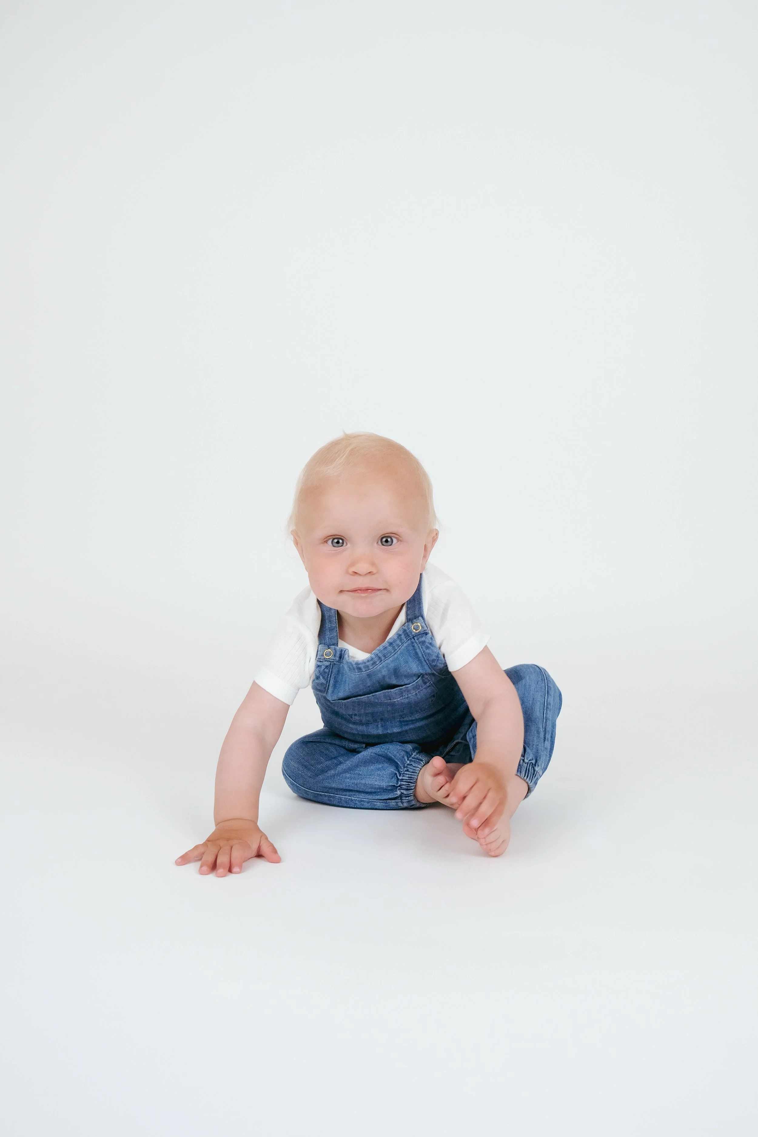 Child in overalls crawling on a white background