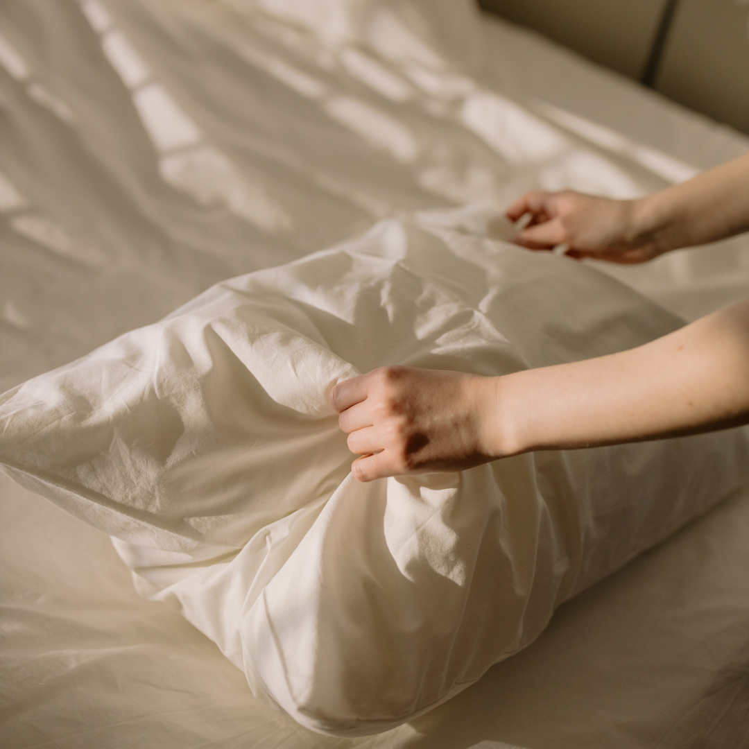 Person smoothing a white bedsheet with their hands on a bed.
