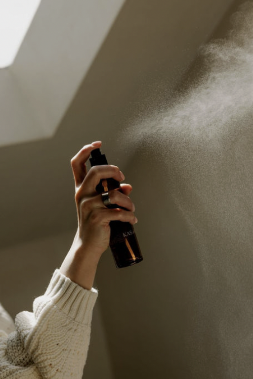 Person spraying a fragrance or mist onto a wall from a black bottle.