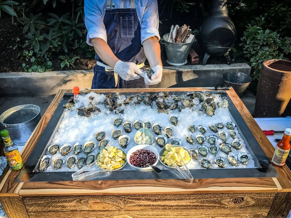 Professional oyster shucker preparing fresh oysters on ice for the oyster bar with oyster mobile experience with garnishes at a mobile oyster bar catering event.