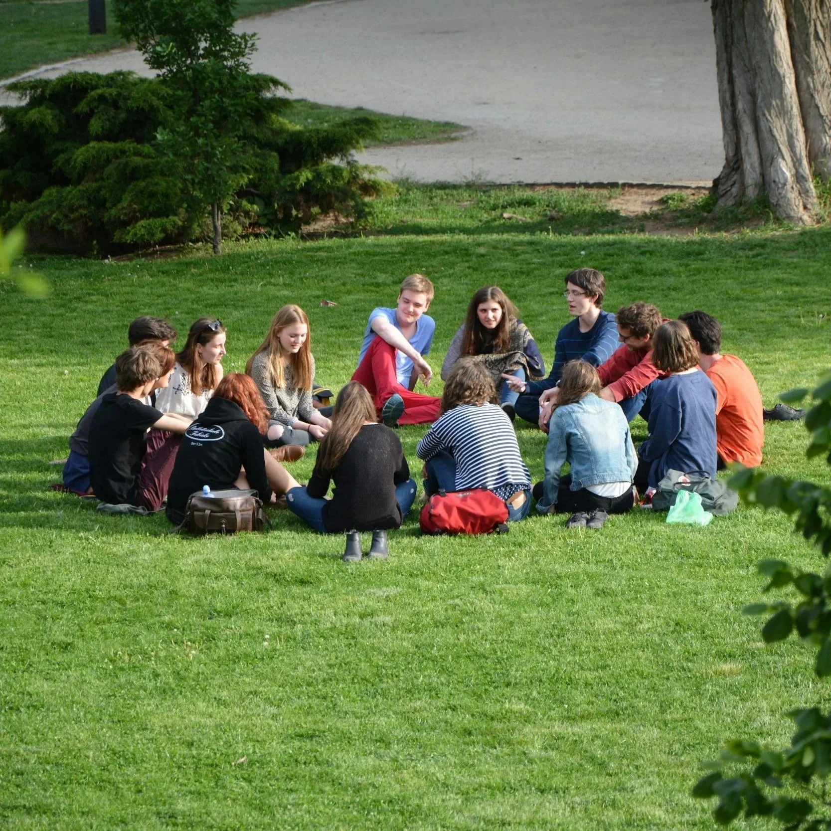 A group of young people sitting in a circle on the grass in a park.