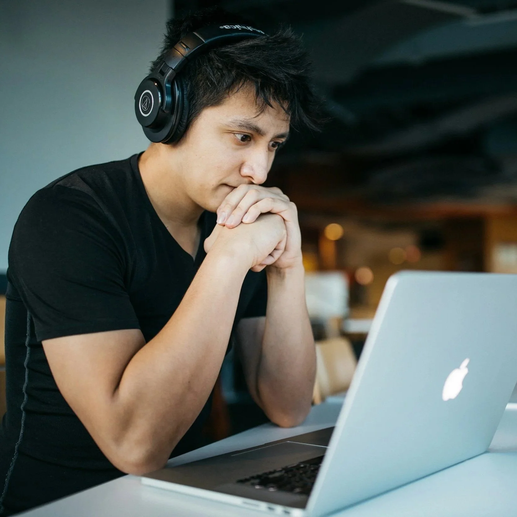 Young man wearing headphones intently working on a silver MacBook while he studies his manual therapy and pain science course online to discover a more modern approach to manual therapy..