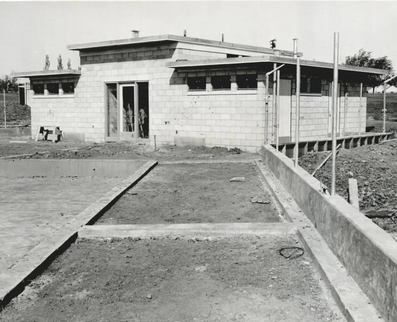 Black and white photo of a house under construction with cinder block walls and unfinished driveway, construction tools and scaffolding present.