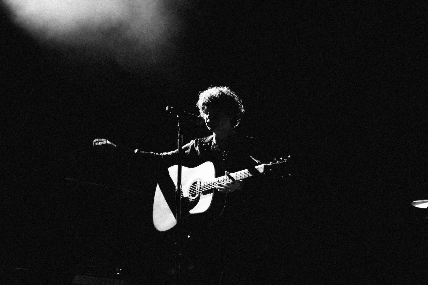 Silhouette of The Kooks lead singer playing guitar and singing into a microphone on a dark stage with spotlight - at Palace Foreshore St Kilda.