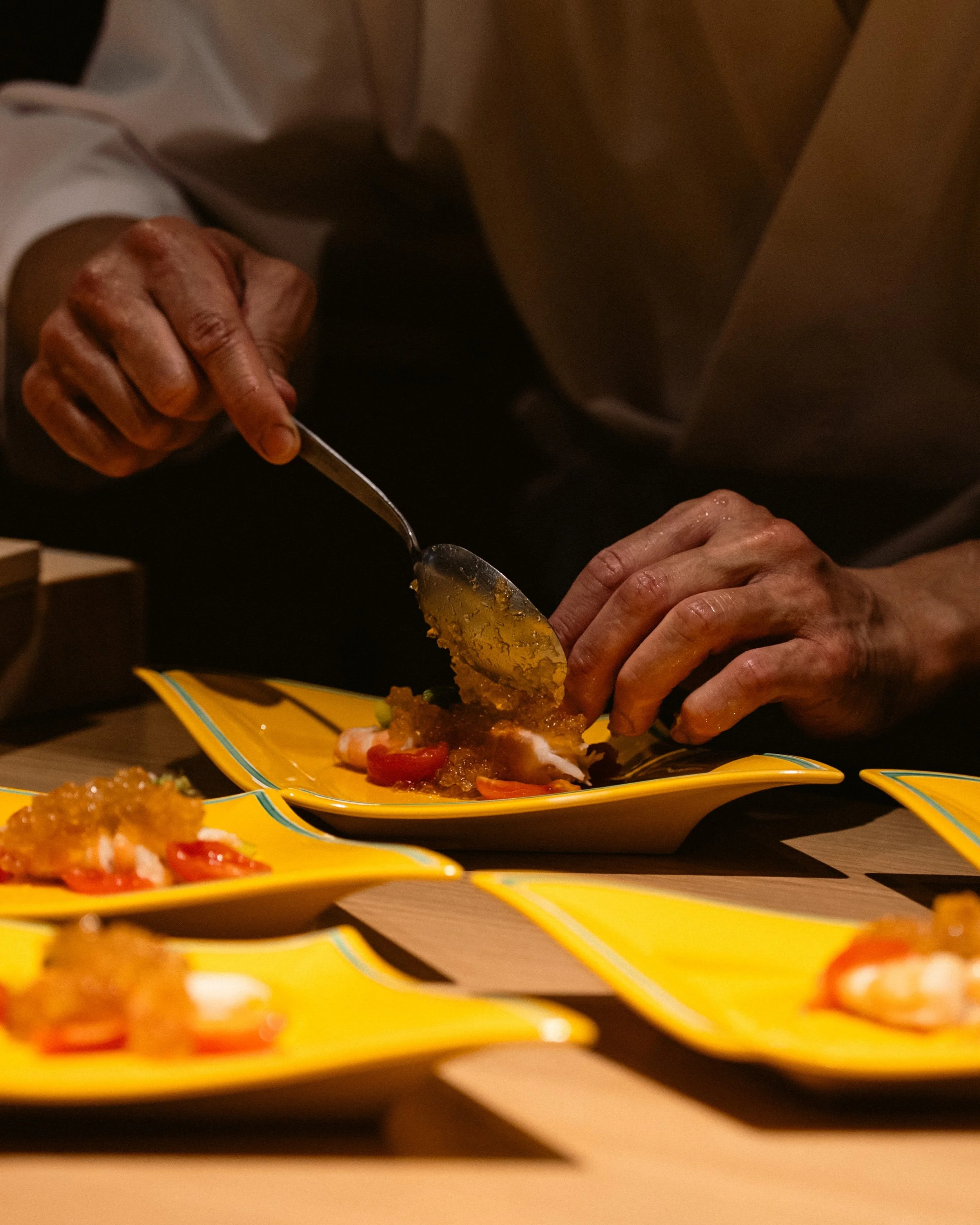 Chef Atsushi using a silver spoon to precisely place a delicate sauce on a multi-course Kaiseki tasting dish.