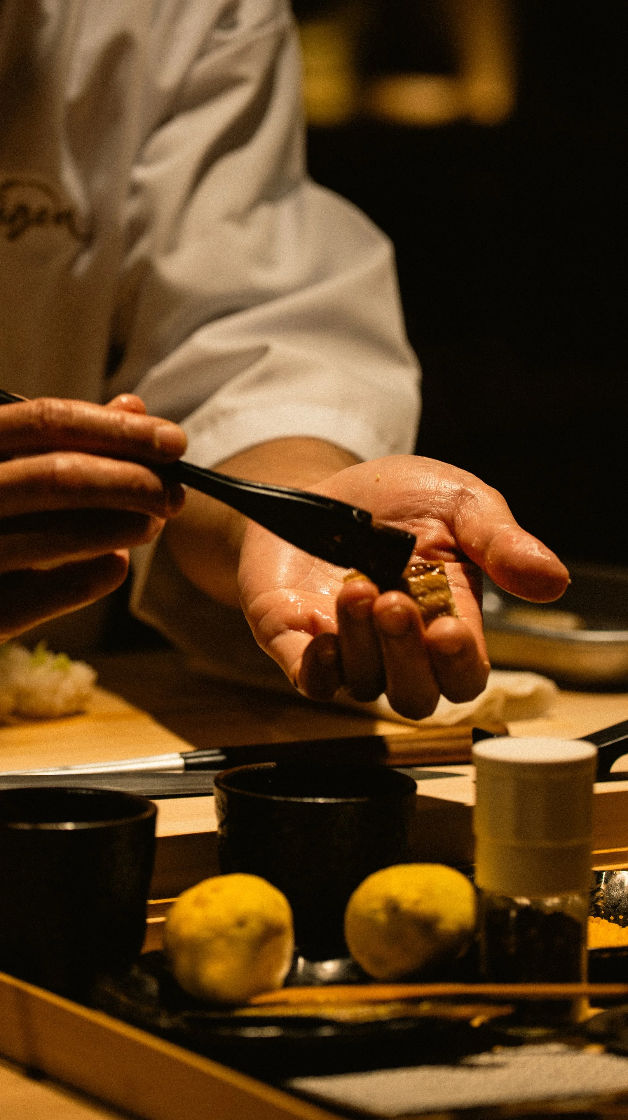 Close-up of Chef Atsushi applying a signature soy glaze to a piece of Otoro nigiri with a traditional brush.