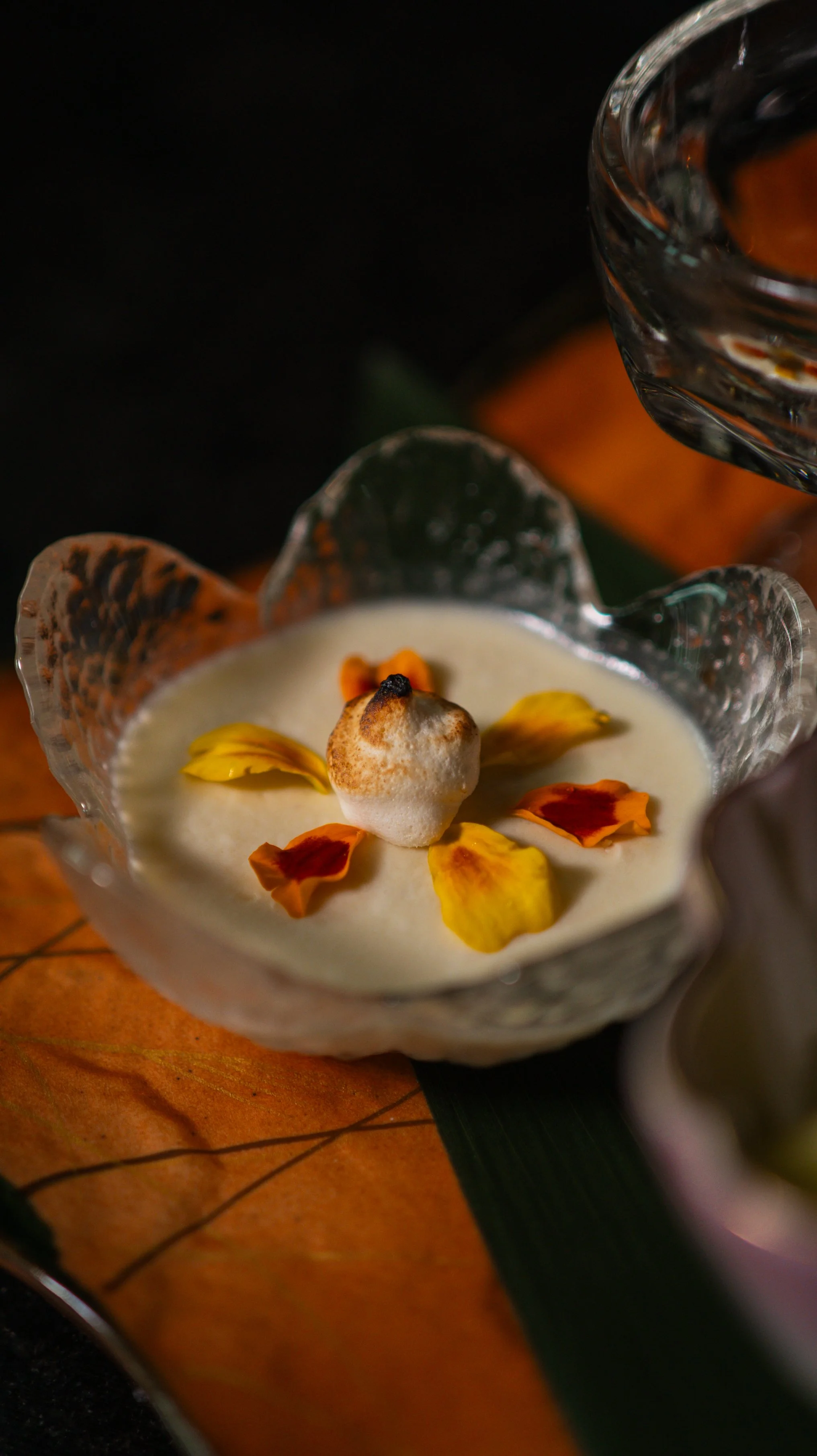 A detailed view of a seasonal Japanese custard dessert topped with edible flower petals and gold leaf.