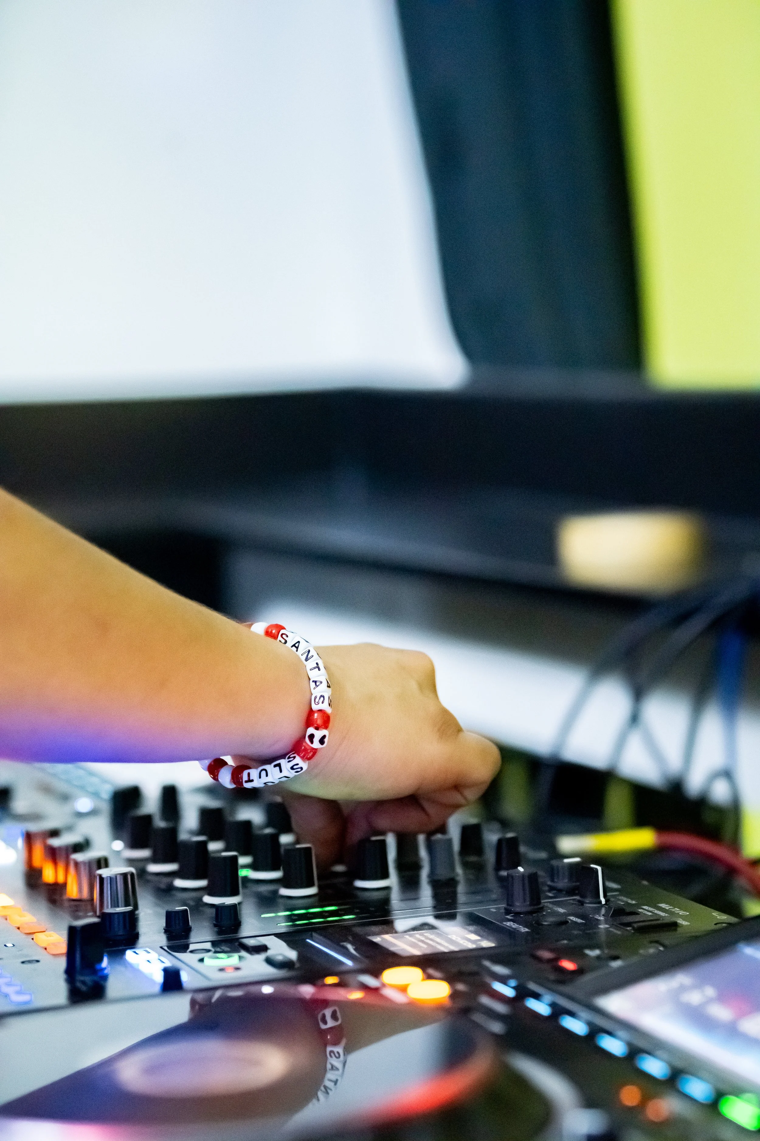 A person’s hand adjusting dials on DJ equipment with a bracelet that has the word 'SANTAS' on it.