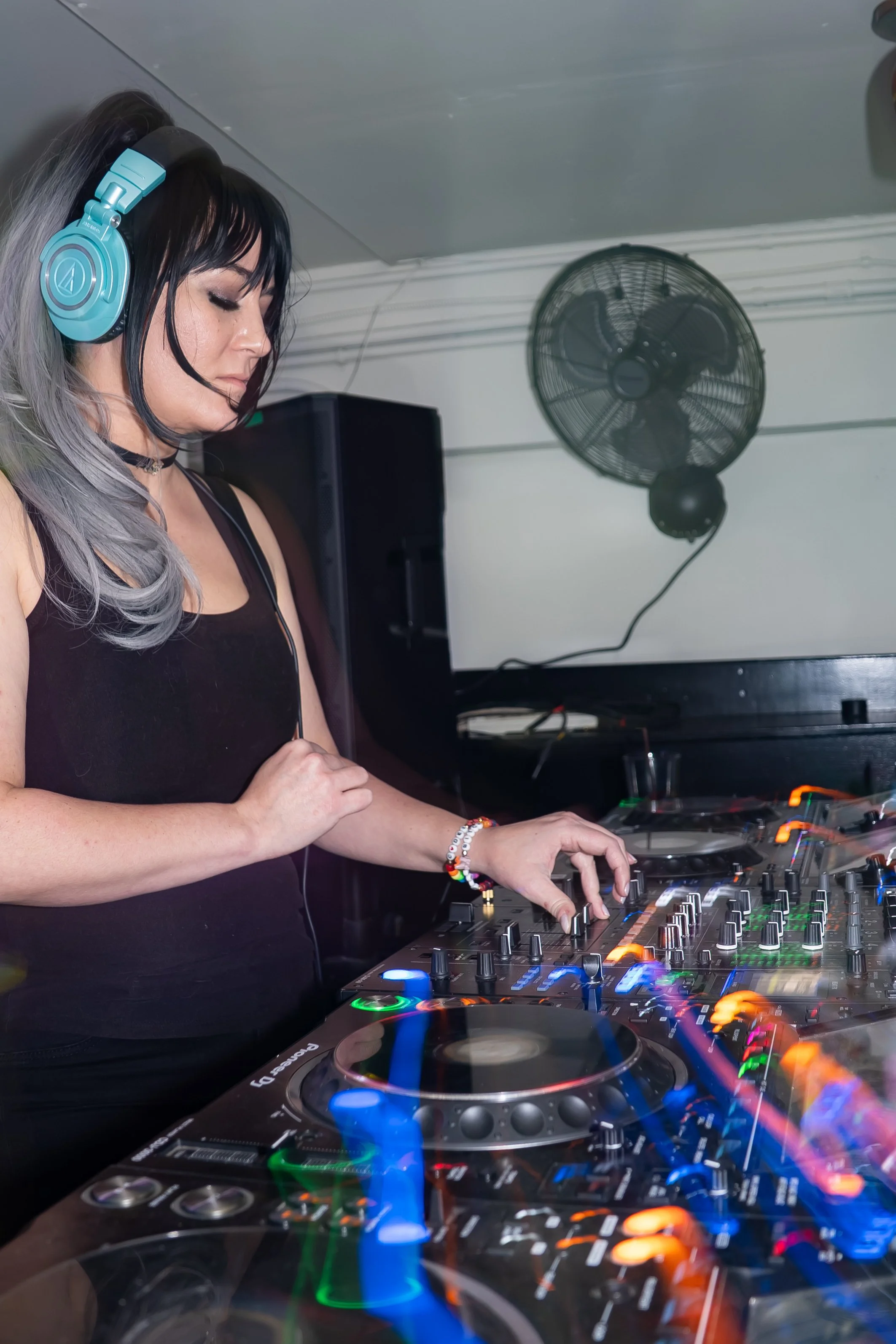 A female DJ wearing headphones playing music at a club or event.