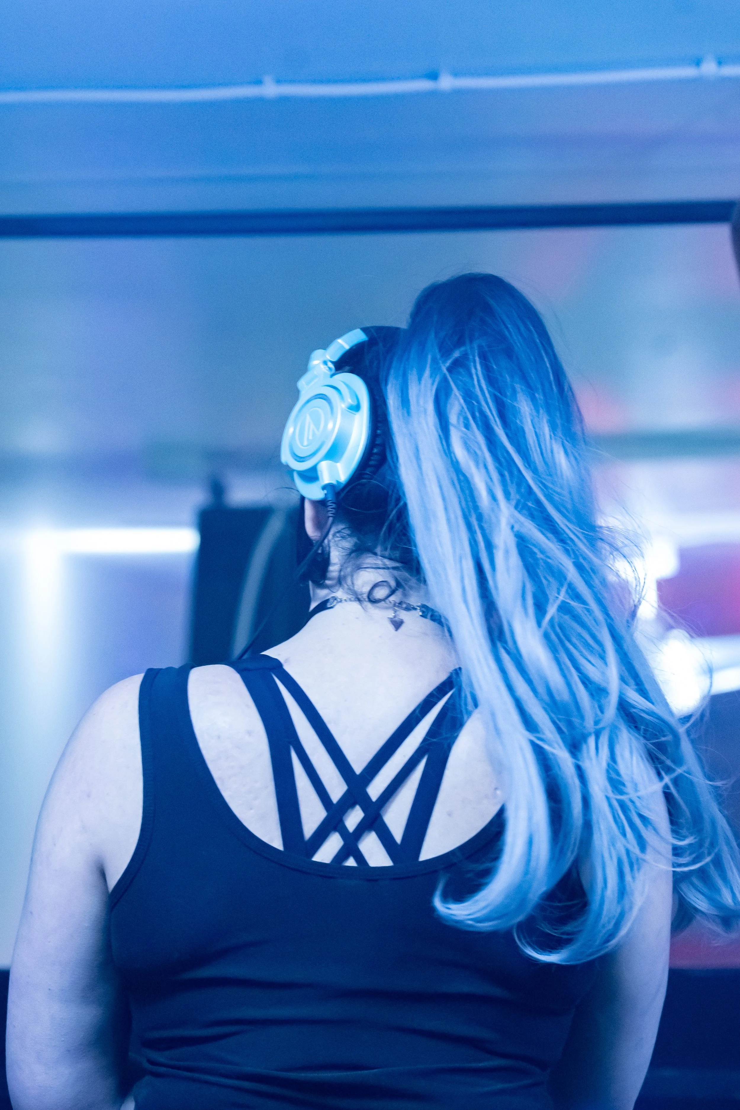 A woman with long hair wearing headphones in a dark room illuminated by blue and purple lights, possibly at a nightclub or concert.