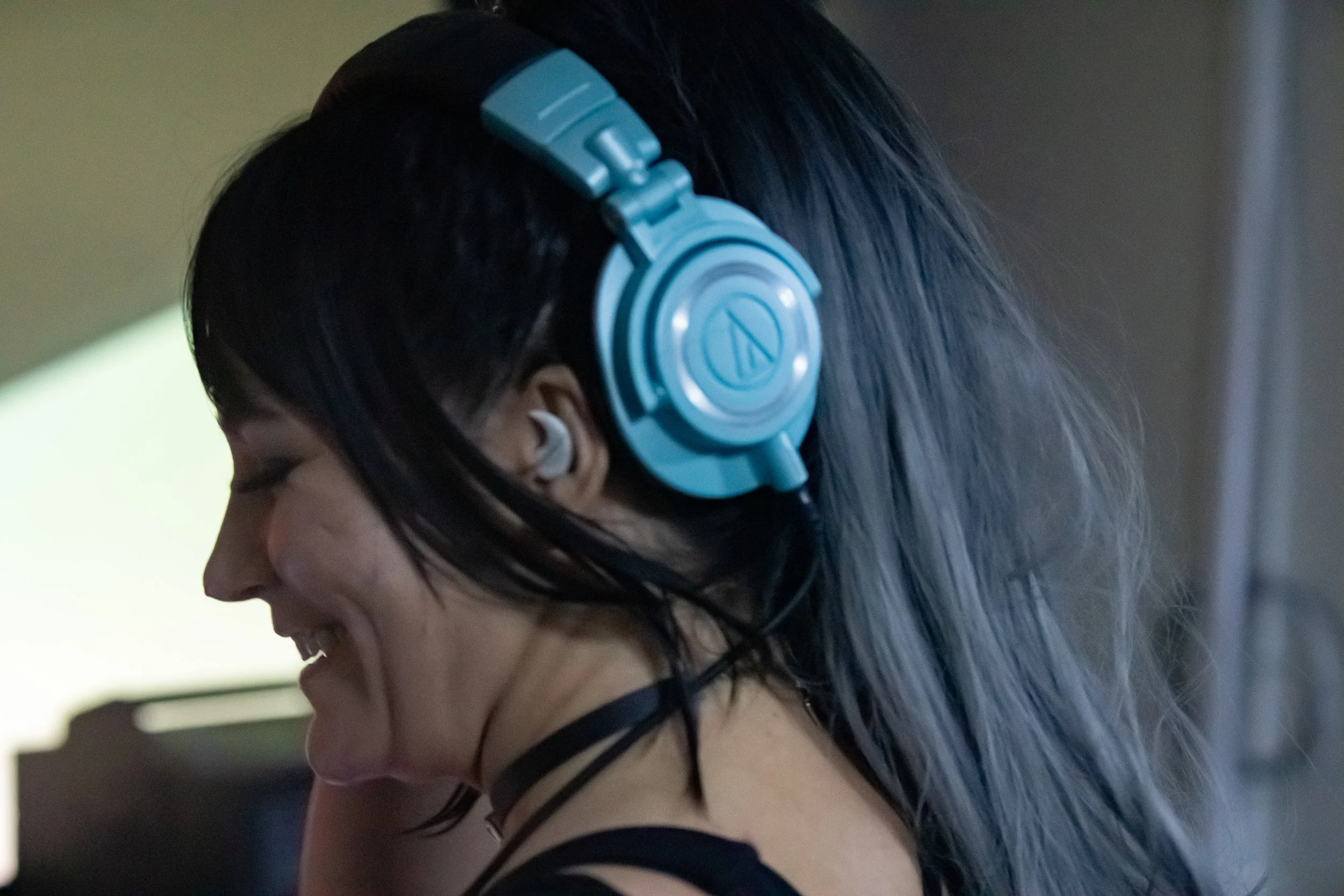 A woman with dark hair wearing a blue headphone and a white earbud, smiling and looking down.