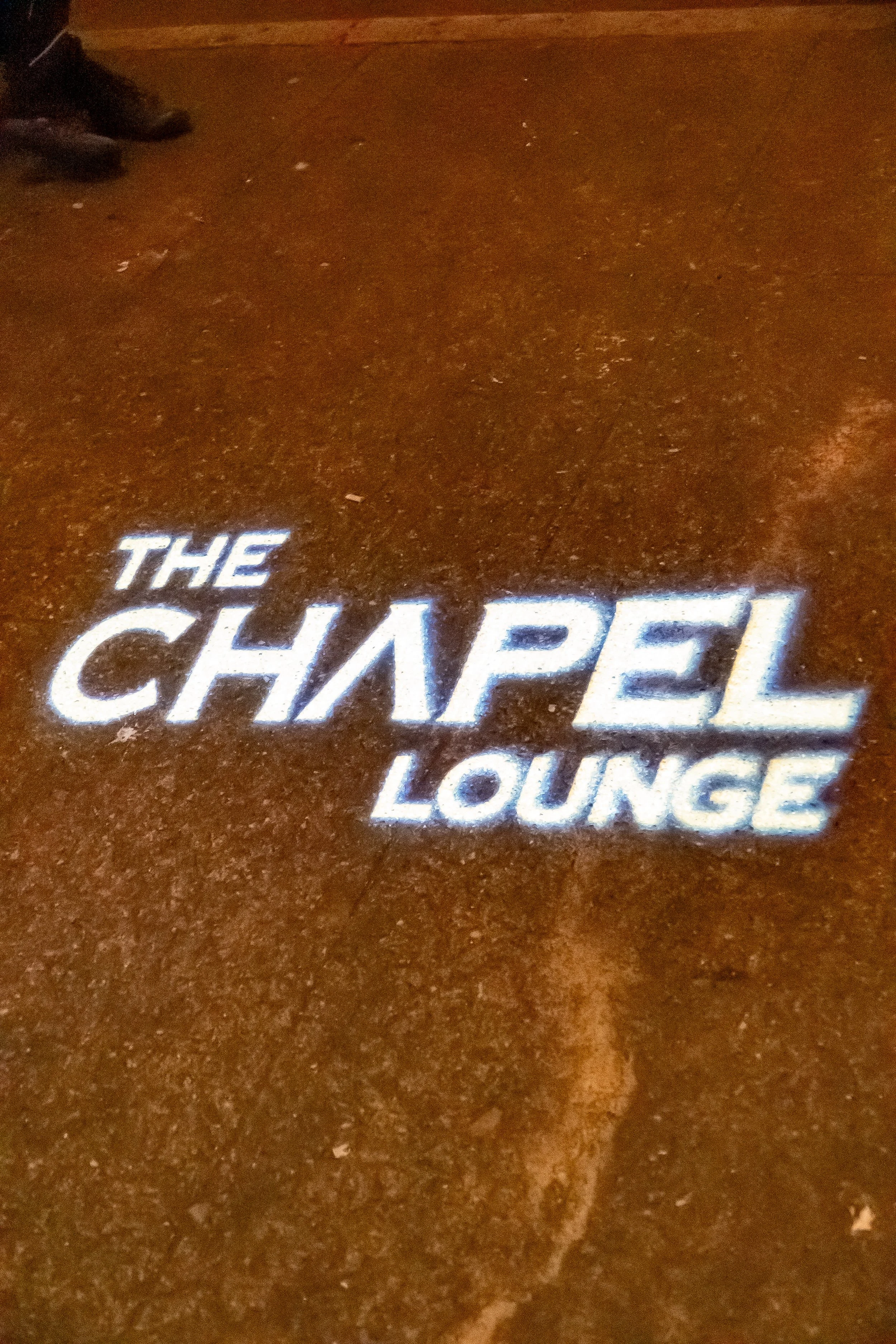 Lighting projection on the floor displaying the text 'The Chapel Lounge' in bright white letters.
