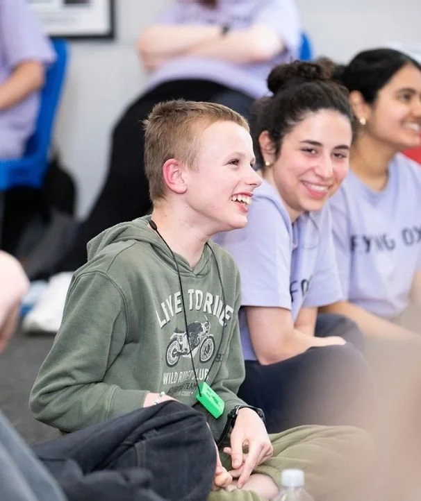 A group of young people sitting together indoors, smiling and laughing, at a magic show.