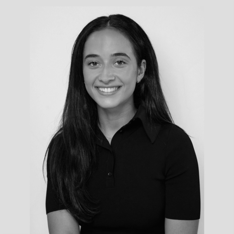 Black and white portrait of a smiling woman with long dark hair, wearing a black shirt, against a plain light background.