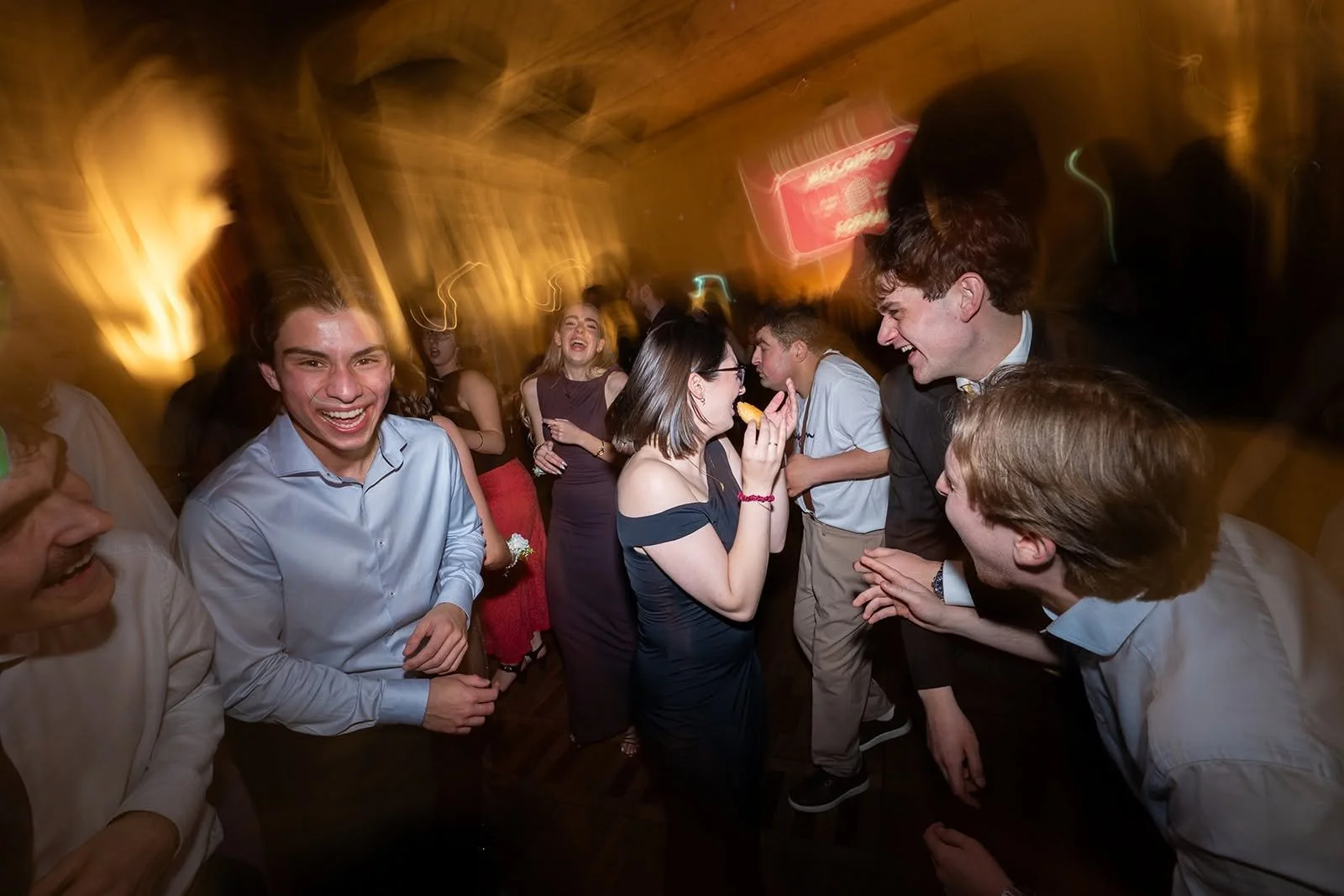 Young adults dancing, laughing, and enjoying a lively party in a dimly lit venue with warm lighting and blurred motion.