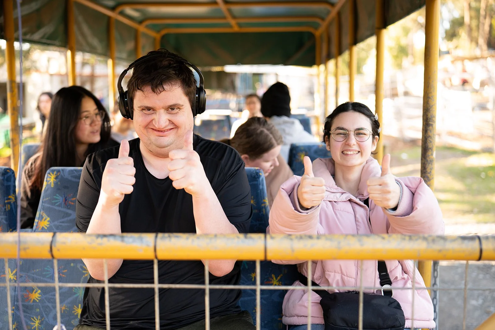 People riding a tour bus, giving thumbs-up, smiling, and enjoying the ride.