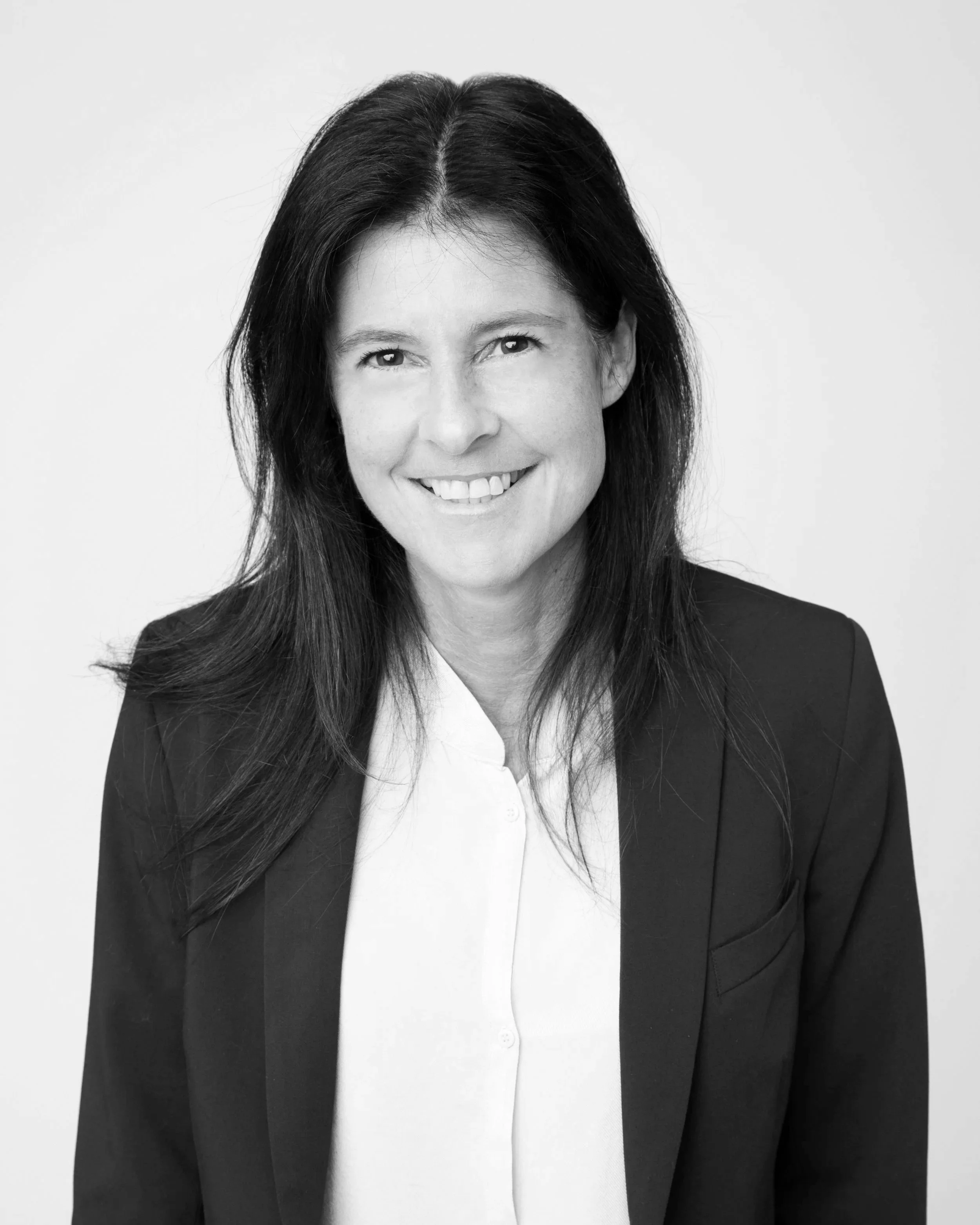 A black-and-white portrait of a woman with dark hair, smiling, wearing a white shirt and a dark blazer.