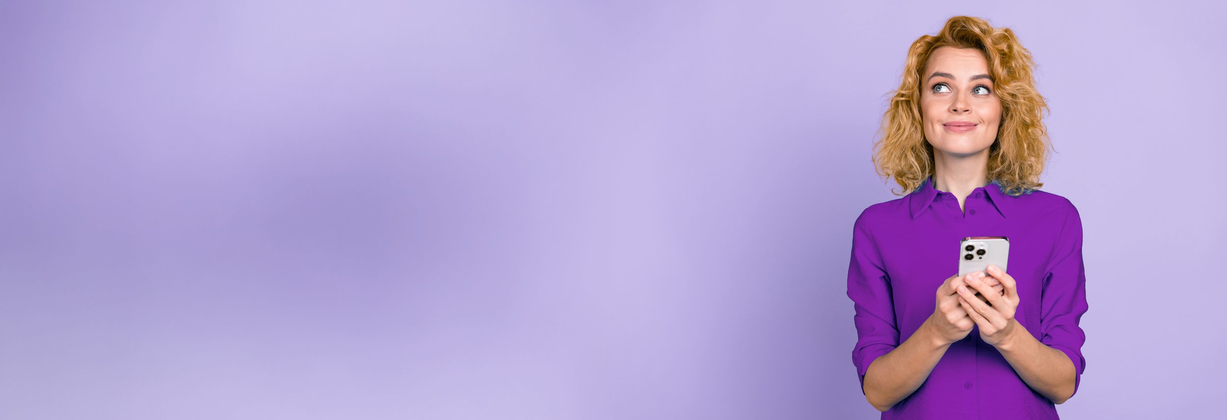 A woman with curly blonde hair wearing a purple blouse holding a smartphone and looking to her right against a lavender background.