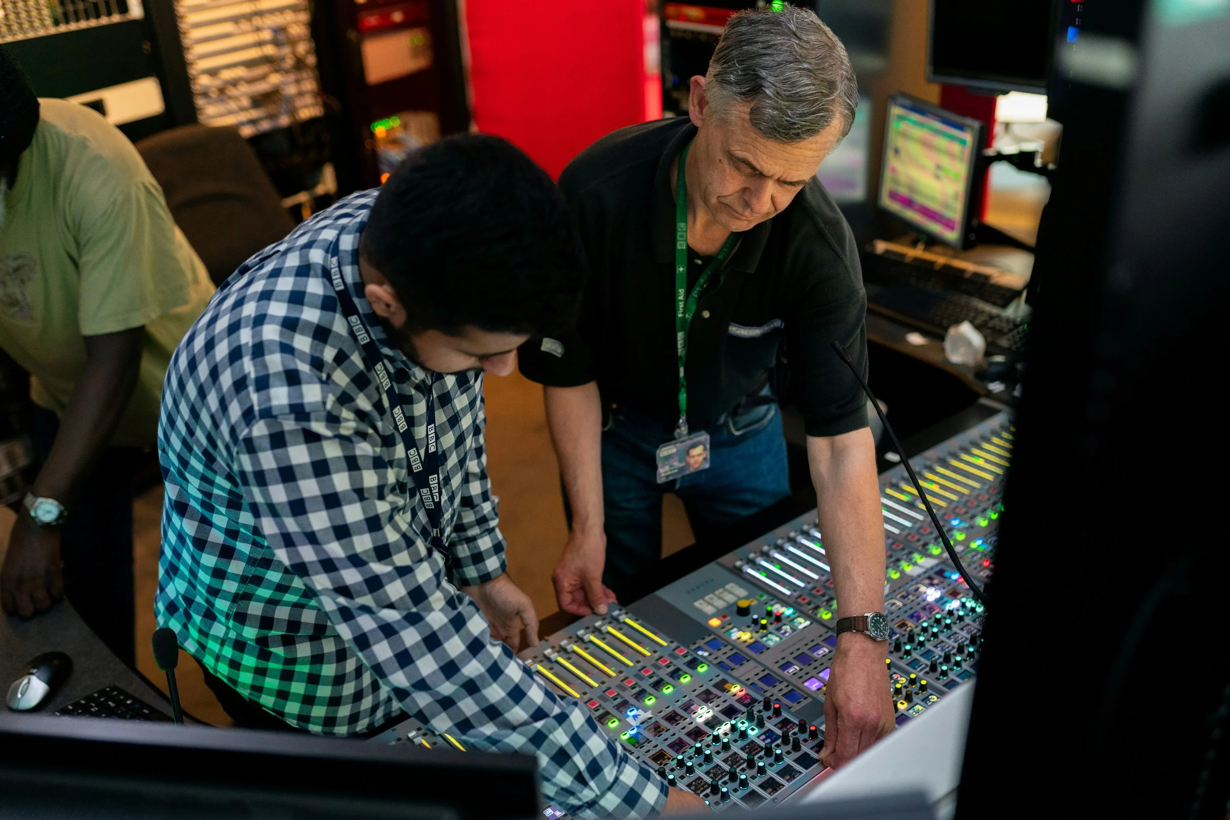 Two men working at a sound mixing console with colorful illuminated dials and sliders in a recording studio or control room.