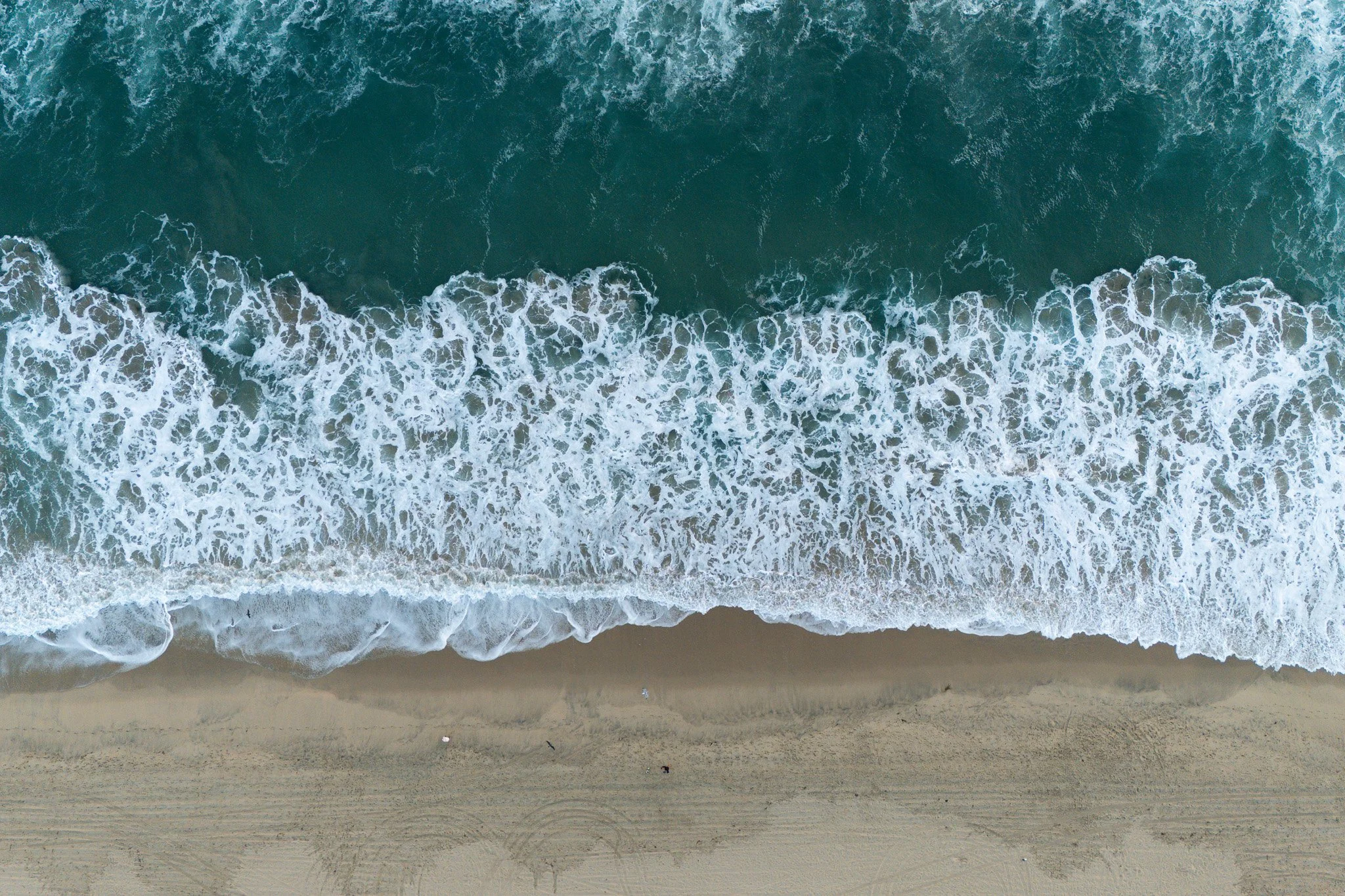 Aerial view of ocean waves crashing onto sandy beach.