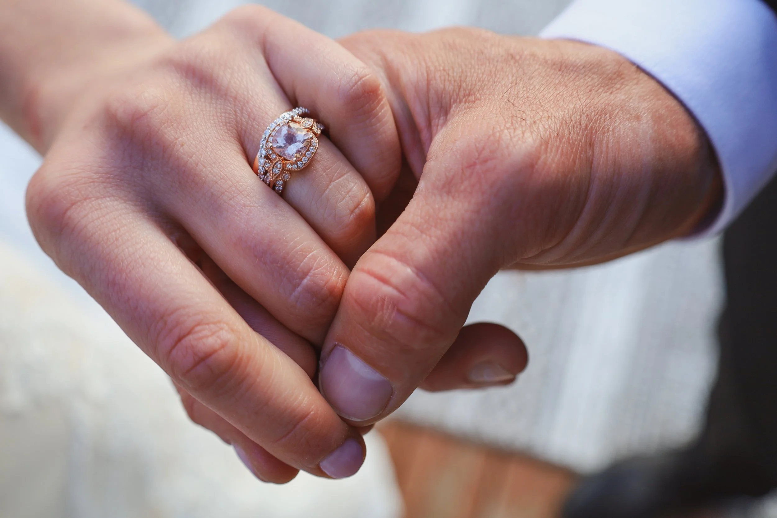 Close-up of a person's hand wearing a decorative engagement ring with a large central gemstone, surrounded by smaller stones, on their ring finger.