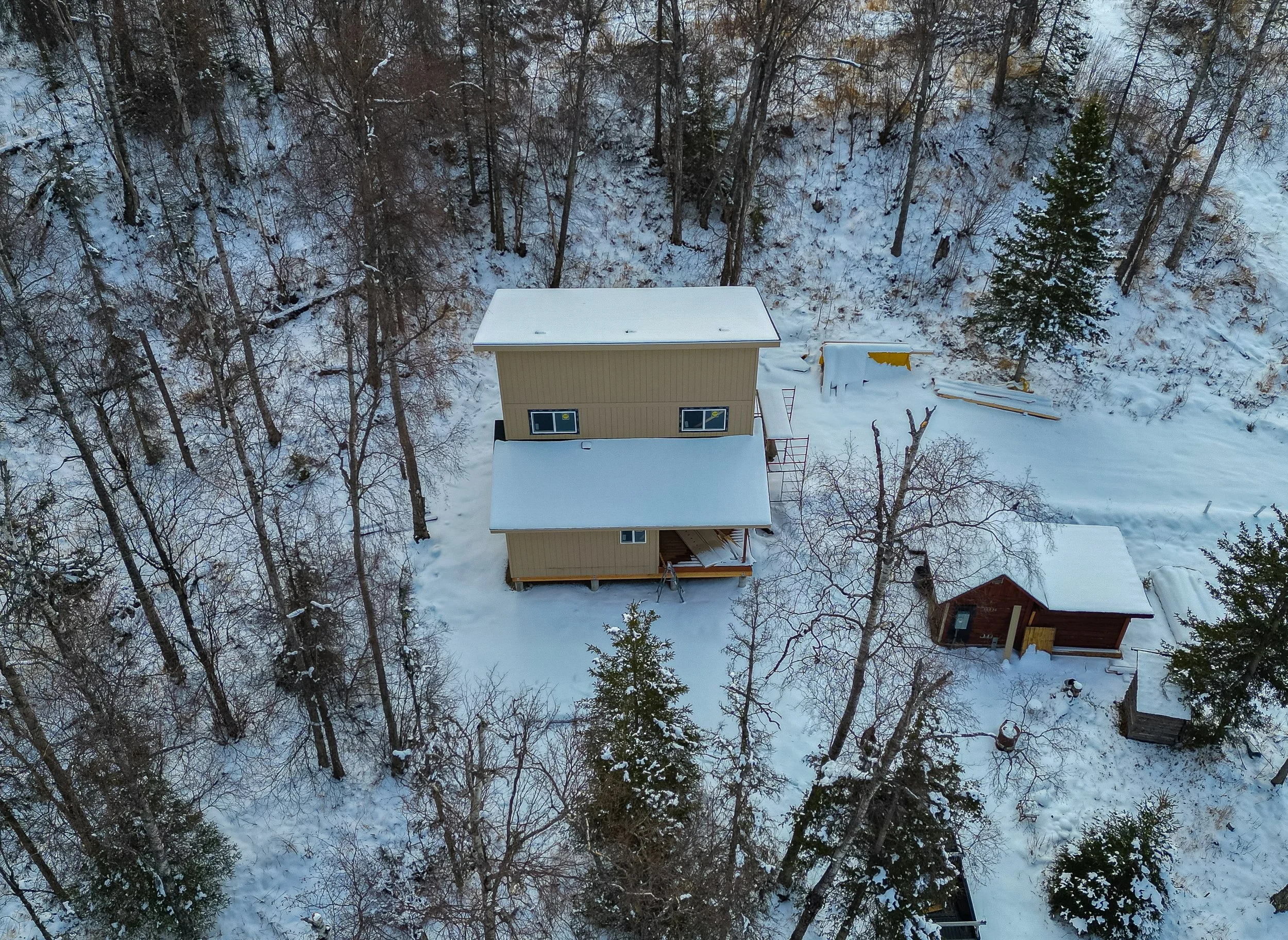 An aerial view of a snow-covered house and surrounding trees in a forested area during winter.