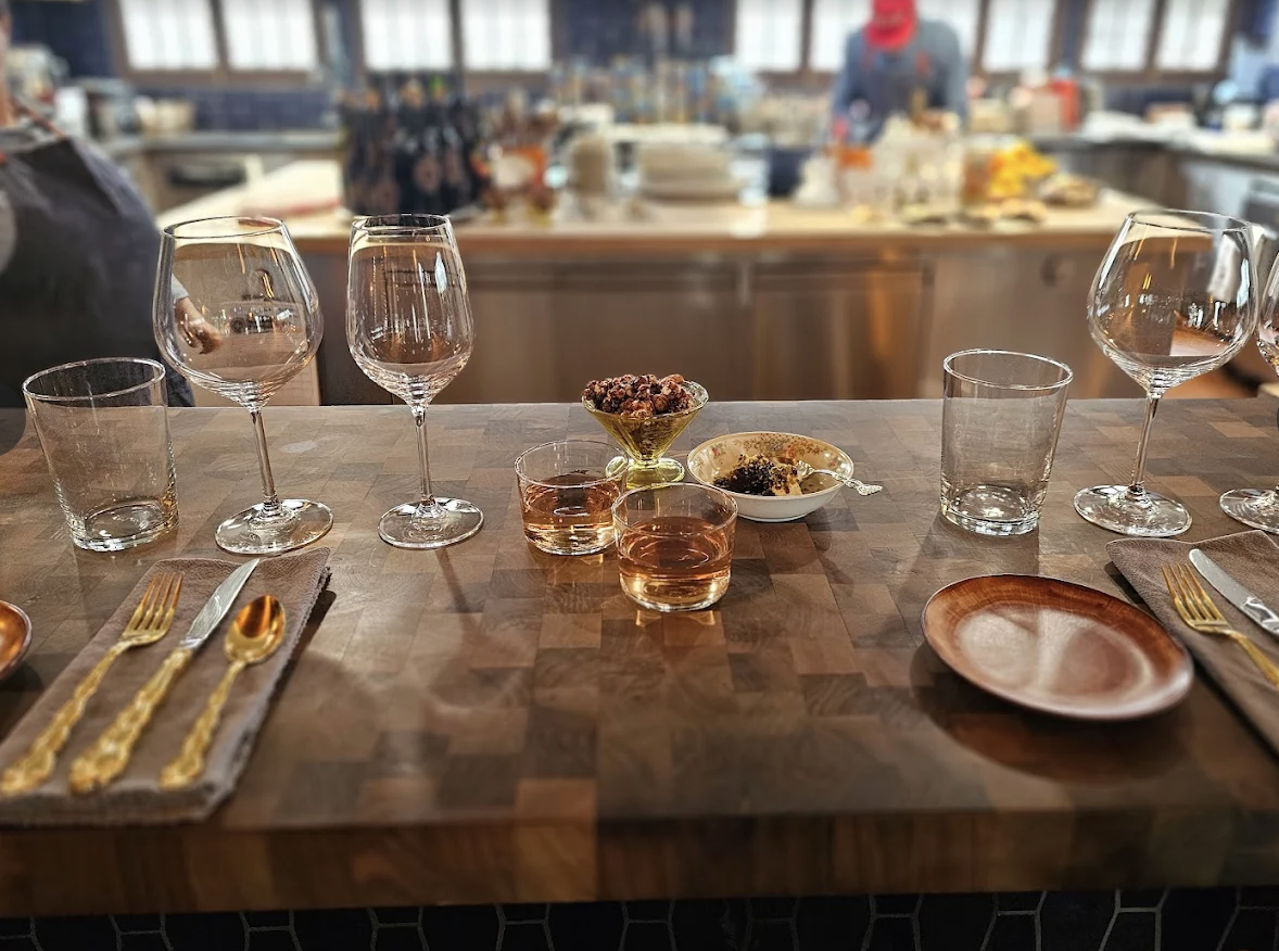 Empty dining table with gold utensils, glasses, and bowls, with a blurred kitchen in the background.